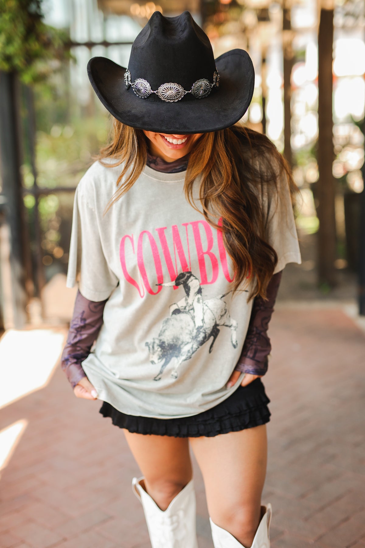 Person wearing a cowboy-themed shirt and black hat outdoors
