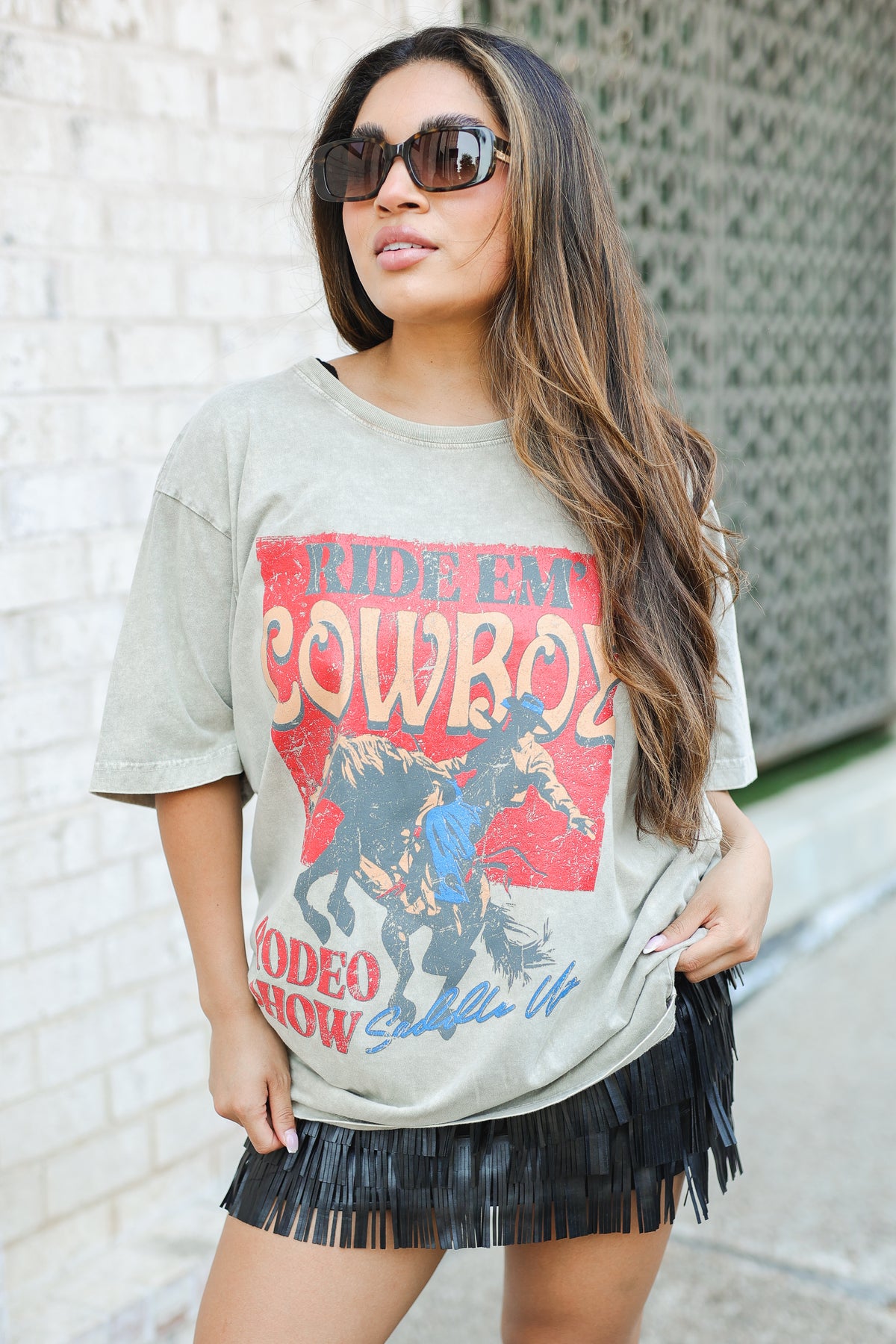 Woman wearing a graphic t-shirt with text and graphics, standing against a light-colored wall.