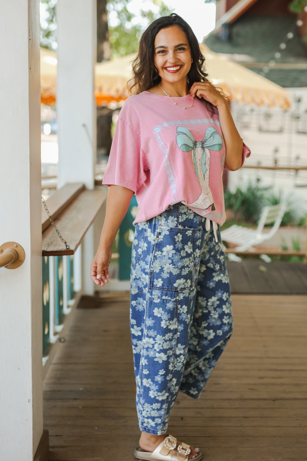 Woman wearing a pink graphic t-shirt and blue floral pants on a wooden deck.