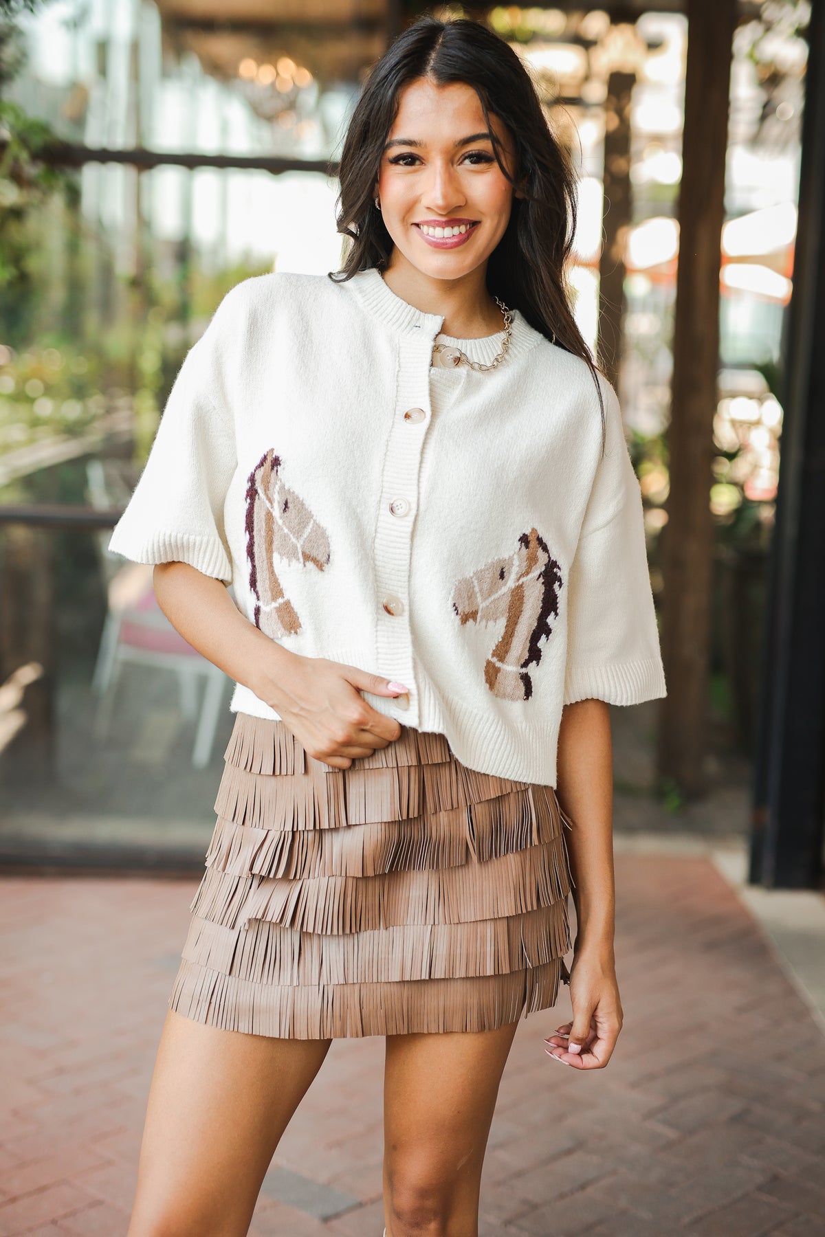 Woman wearing a white blouse with brown patterns and a layered skirt outdoors.
