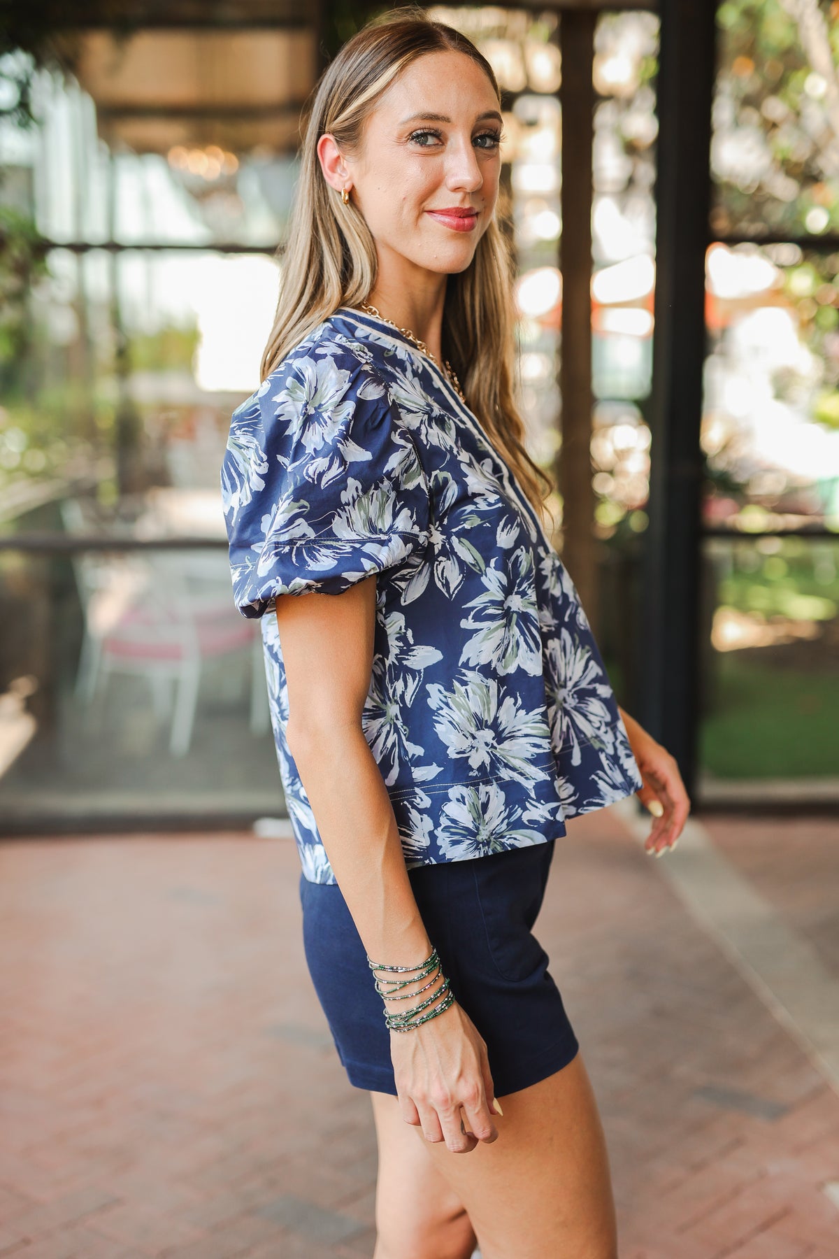 Woman wearing a blue floral top and navy shorts outdoors.