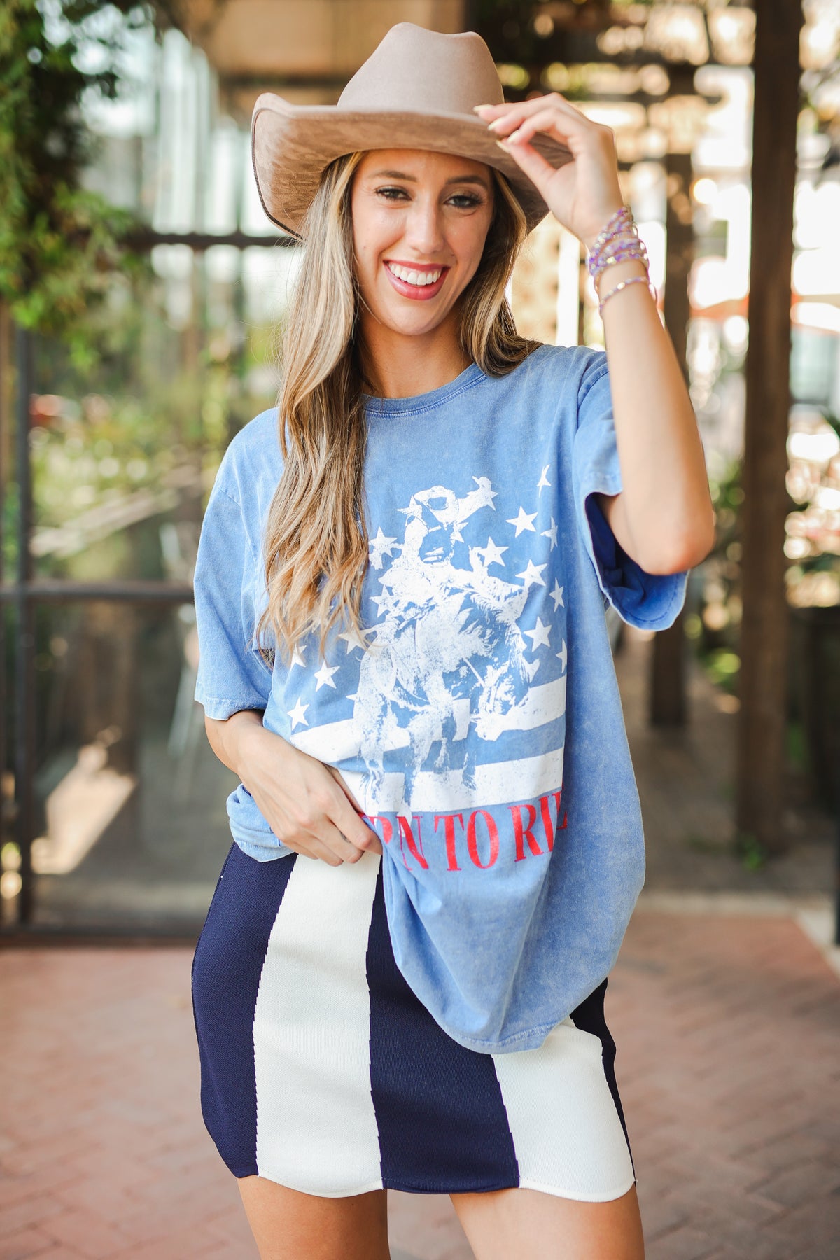 Woman wearing a blue t-shirt with a graphic design and text, navy shorts, and a beige hat.