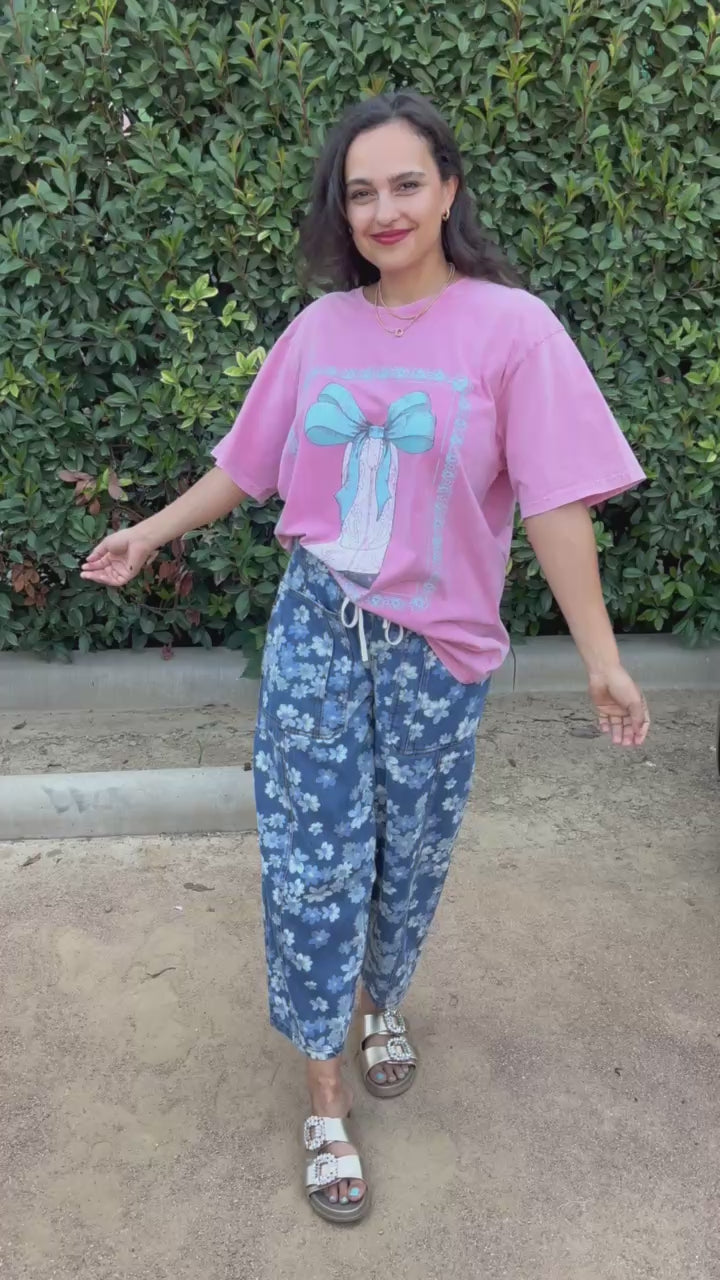 Woman wearing a pink graphic tee and blue pants in an outdoor setting. Southern House Clothing