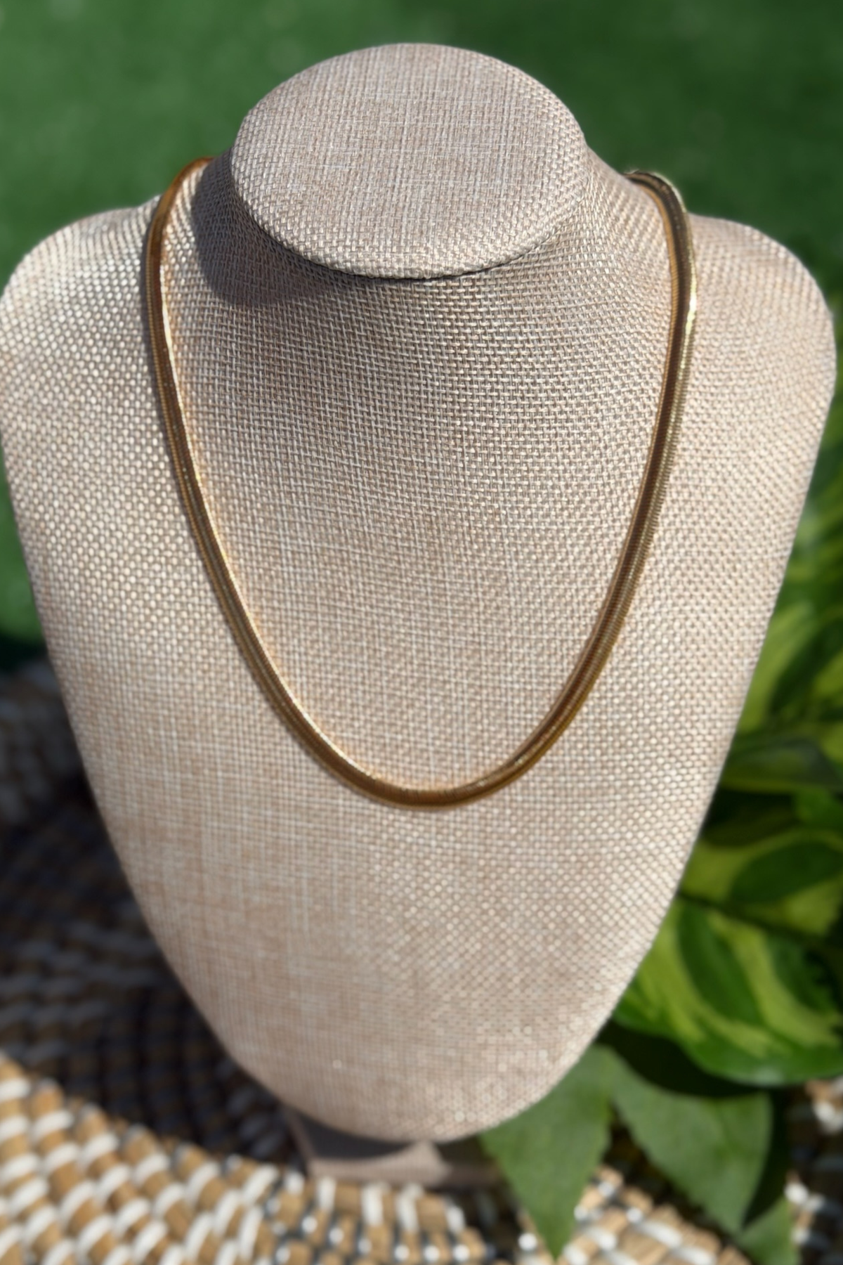 Gold necklace on a beige mannequin bust with a green leafy background