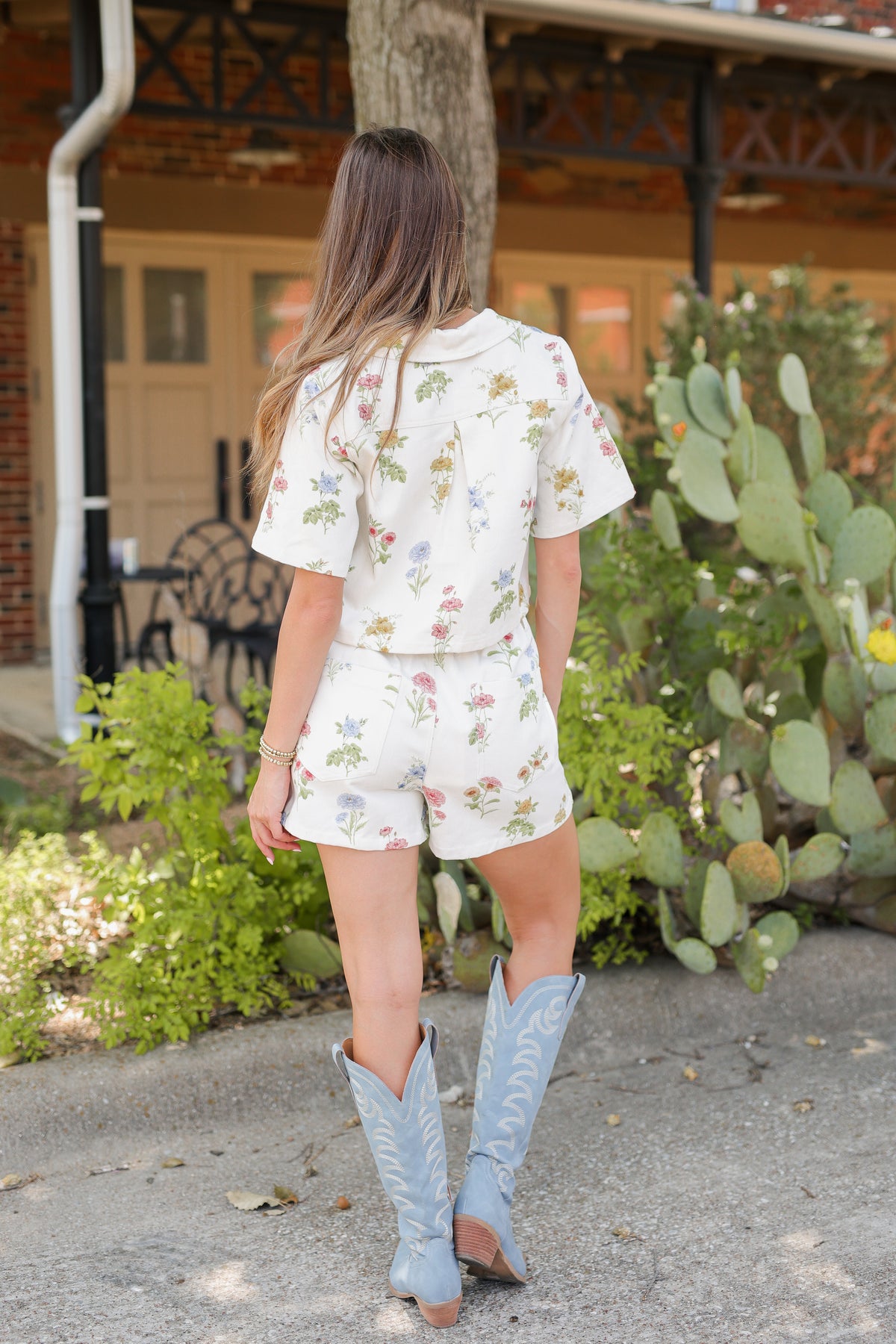Woman in a floral romper and cowboy boots standing in a garden with cacti.
