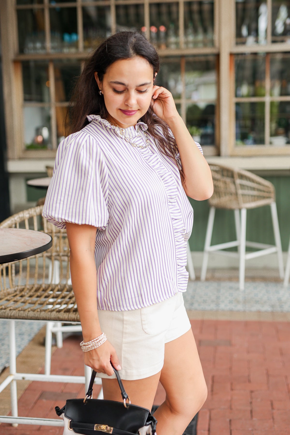 Woman in a striped shirt and shorts standing outdoors near tables and chairs.