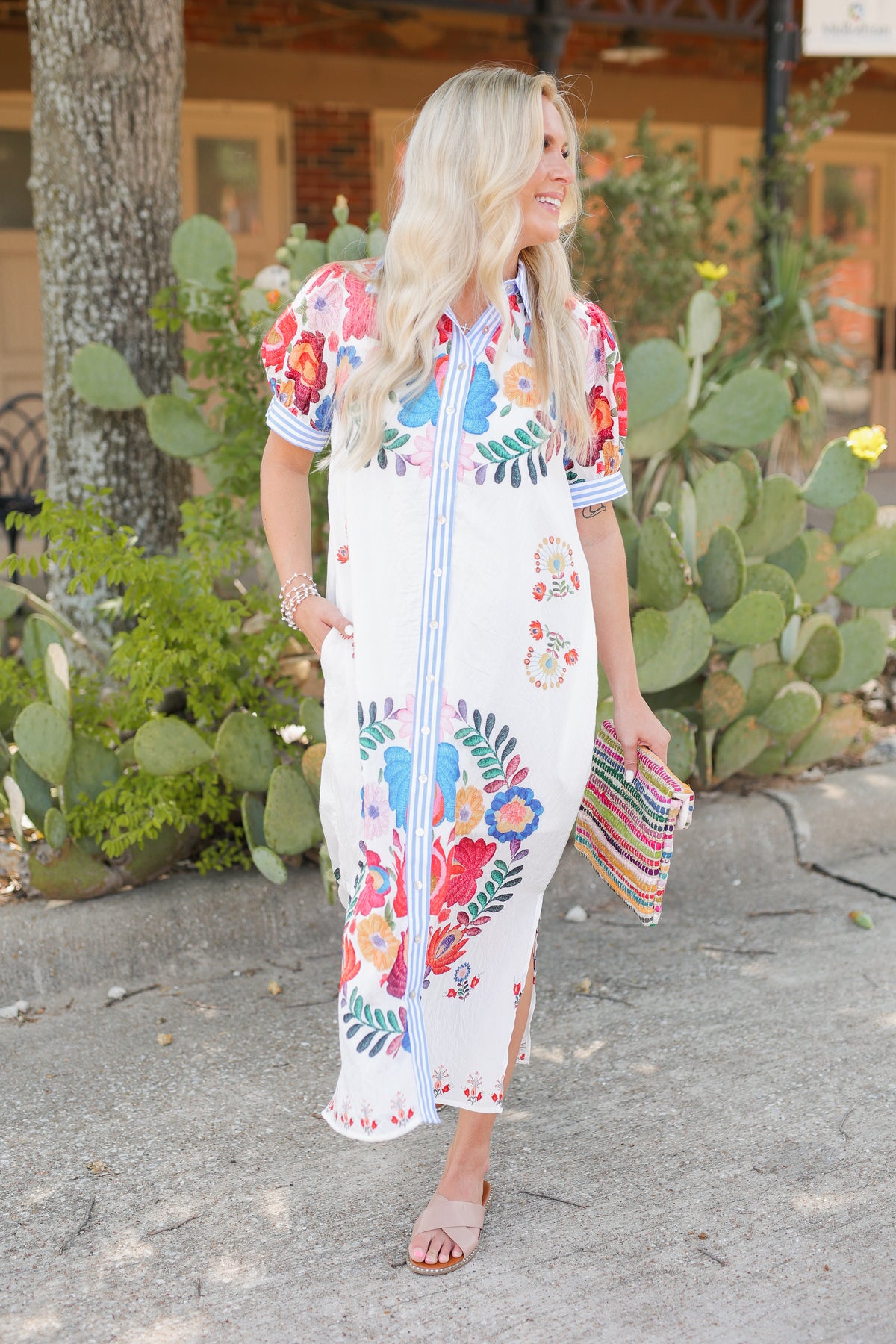 Blonde model is a ivory multi-colored dress standing outside.