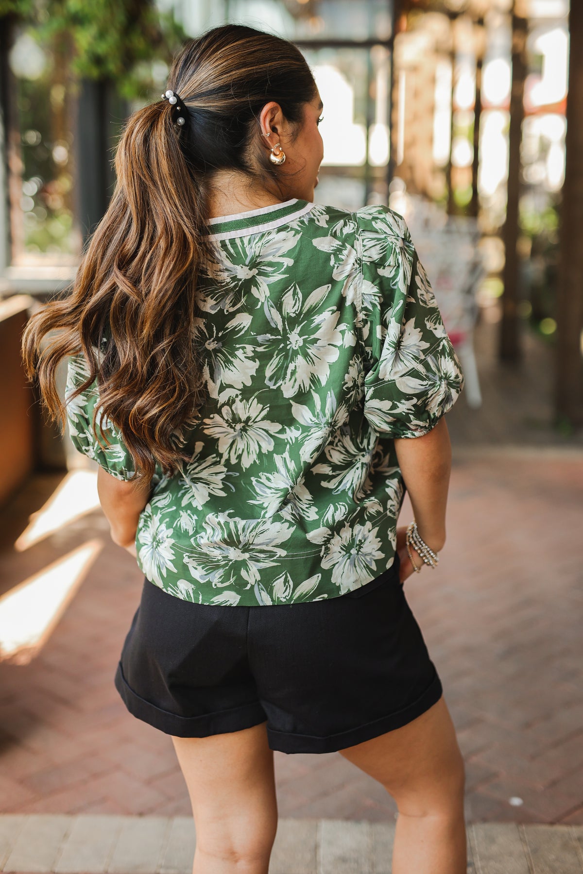 Woman wearing a green floral shirt and black shorts outdoors