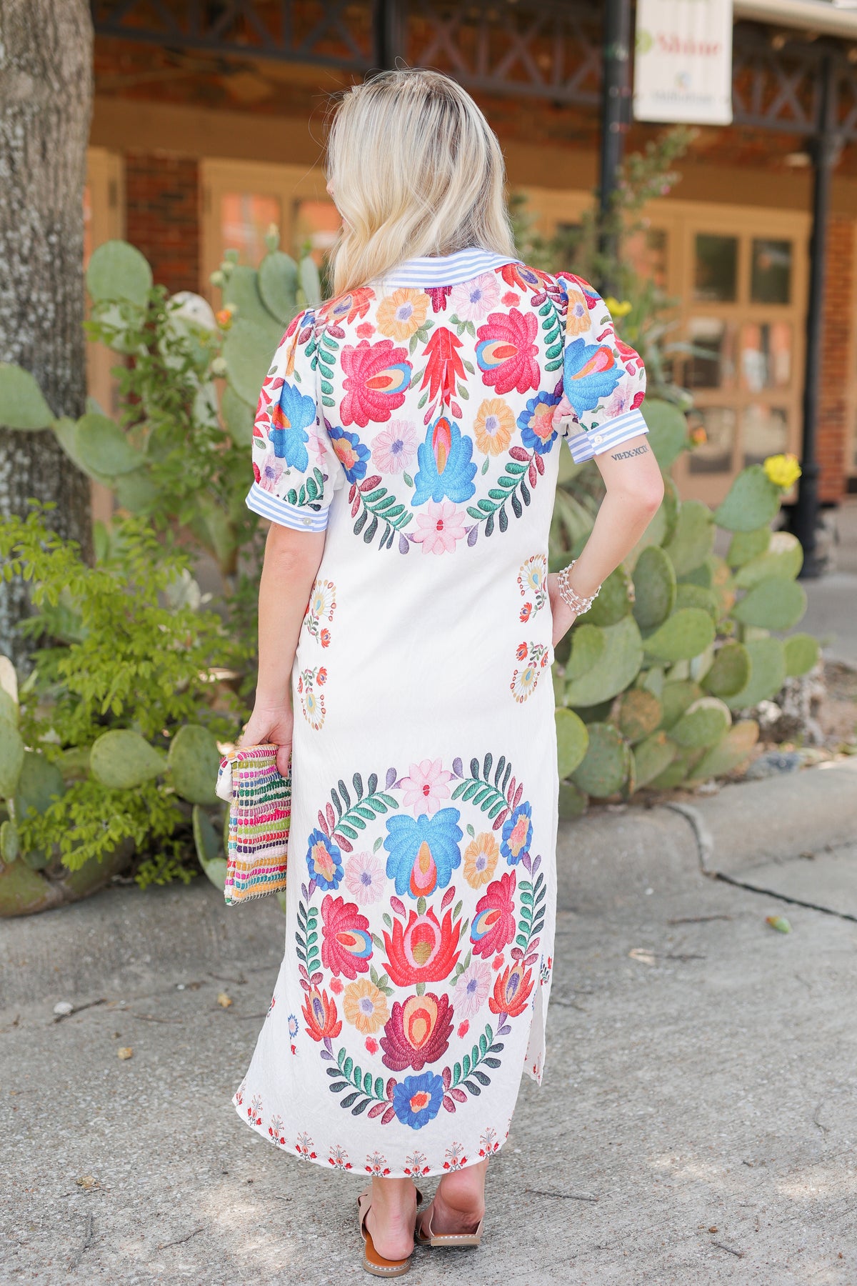 Blonde model is a ivory multi-colored dress standing outside.