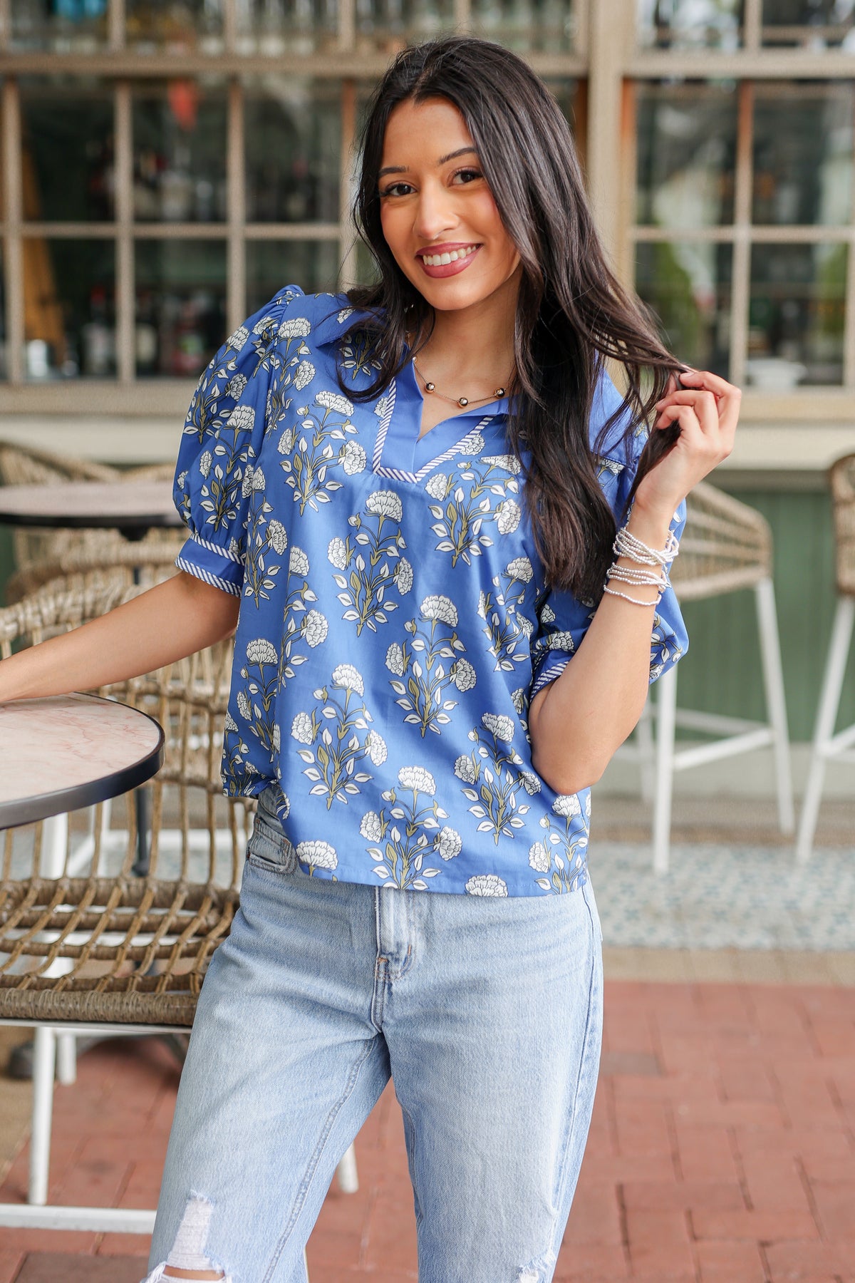 Woman wearing a blue floral blouse and light blue jeans standing outdoors.