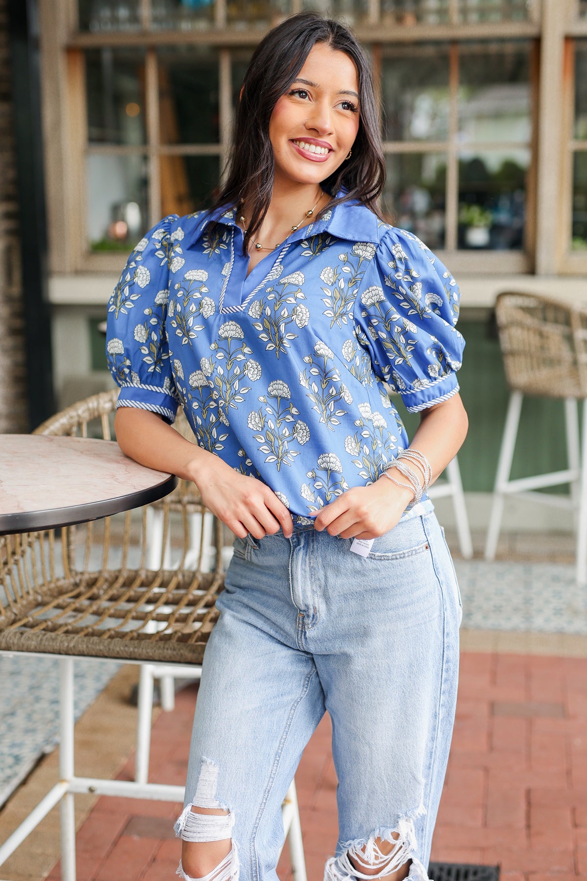 Woman wearing a blue floral blouse and light blue jeans standing outdoors.
