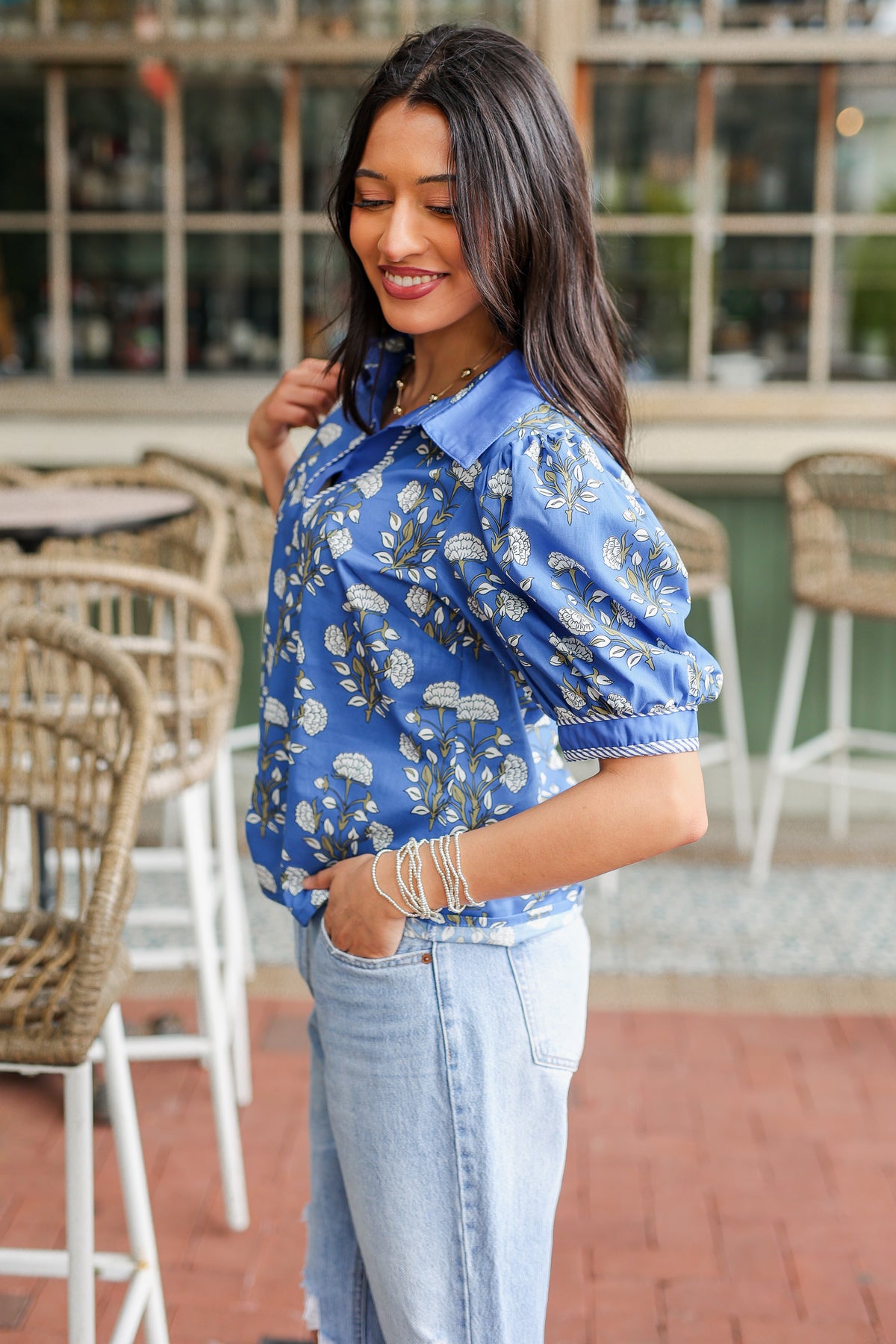 Woman wearing a blue floral blouse and light blue jeans in an outdoor setting.