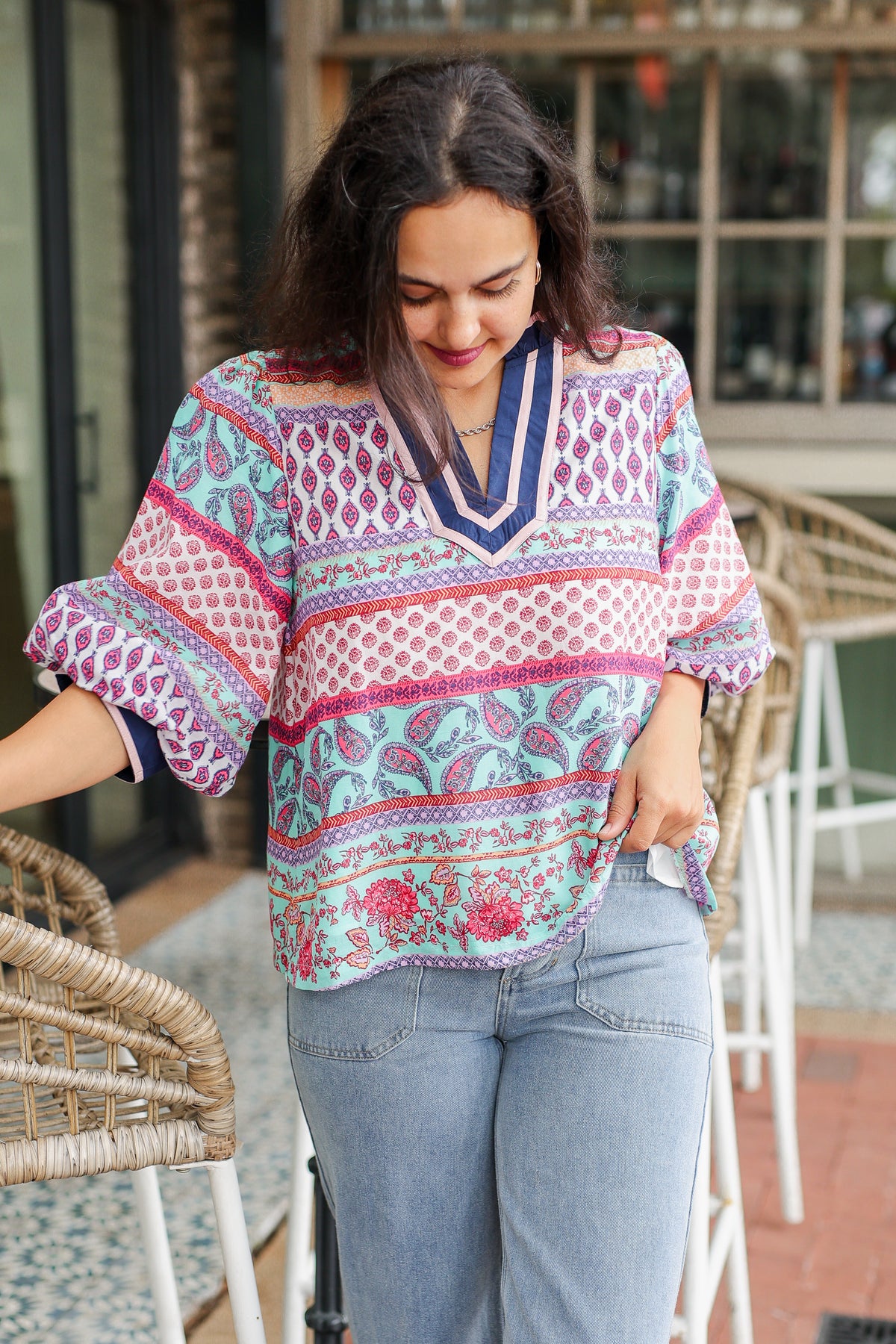 Woman wearing a colorful patterned blouse and jeans outdoors.