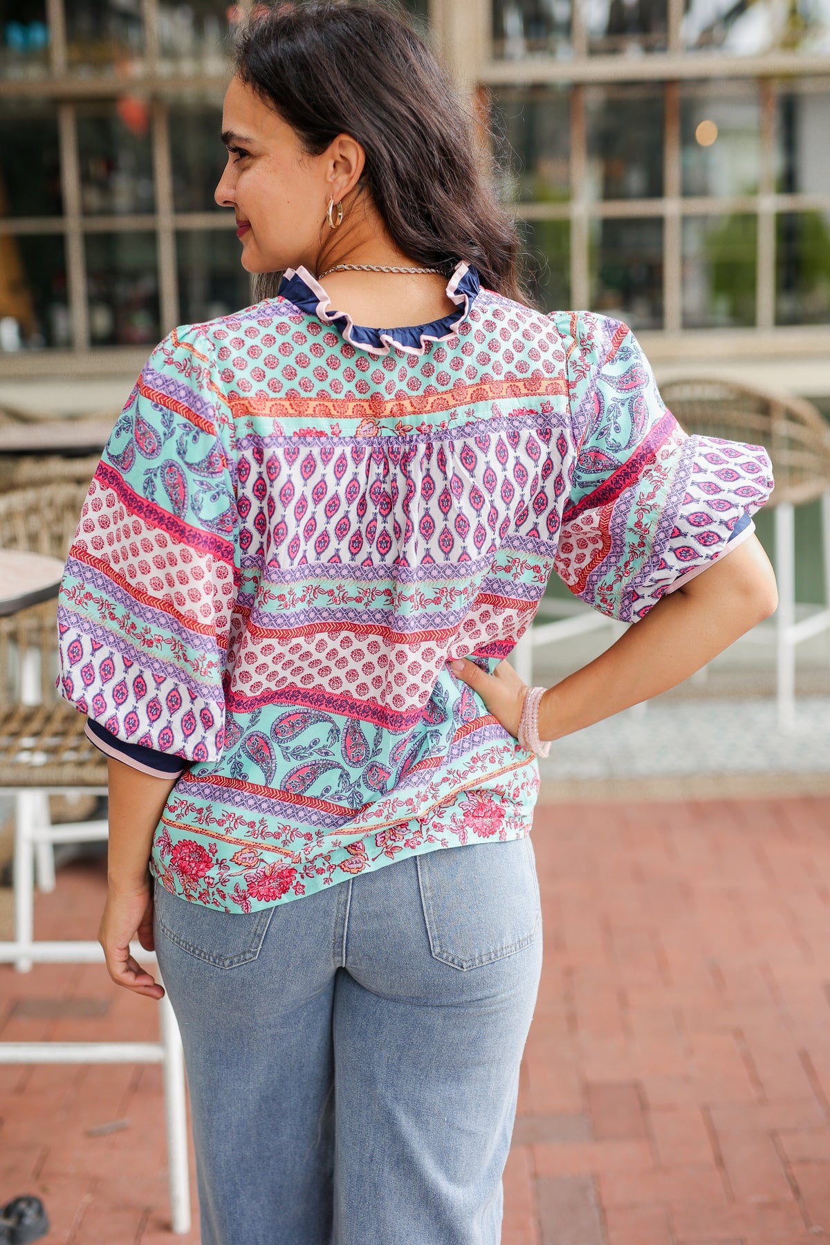 Woman wearing a colorful patterned blouse with blue jeans outdoors.
