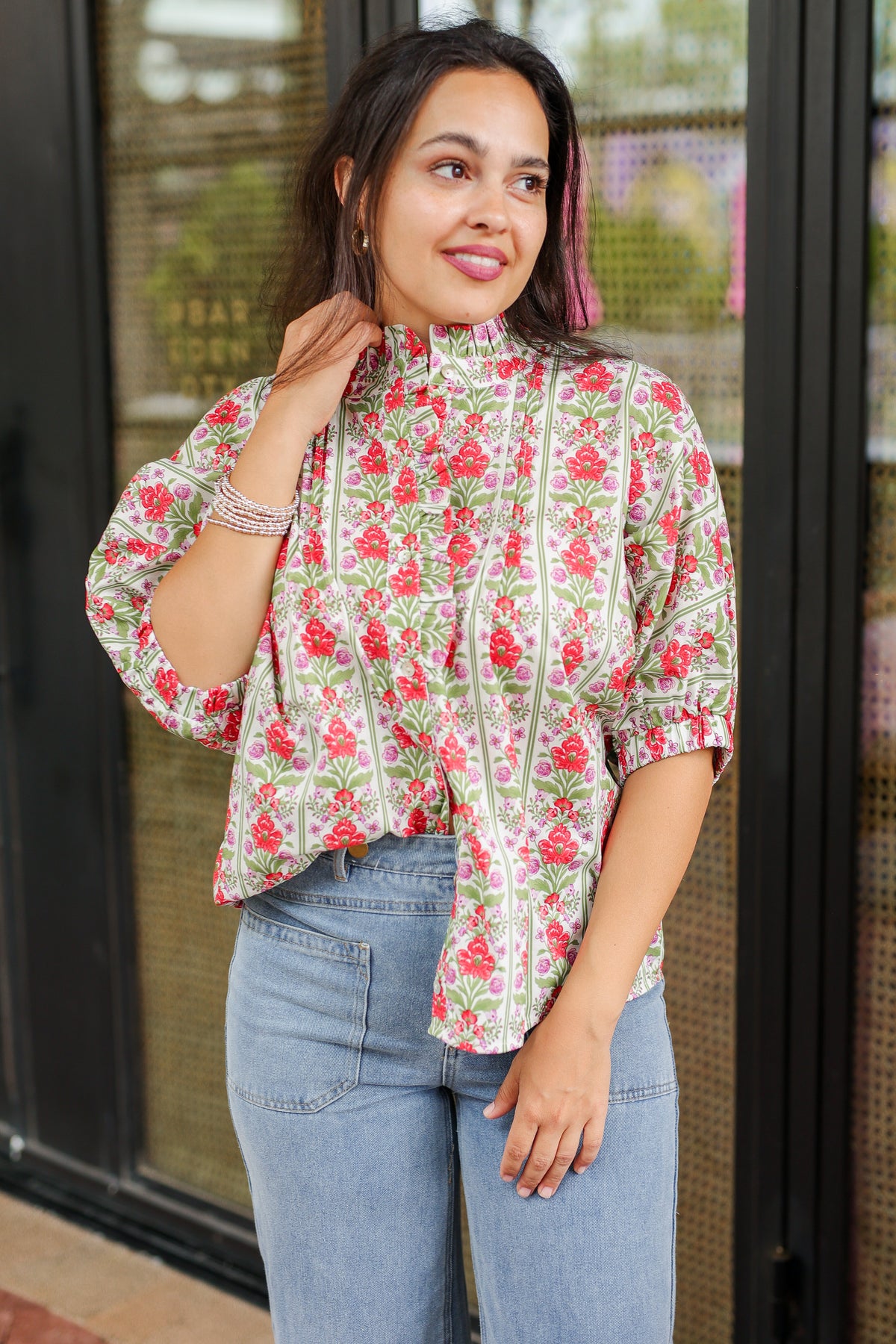 Woman wearing a floral blouse and jeans standing in front of a store entrance.