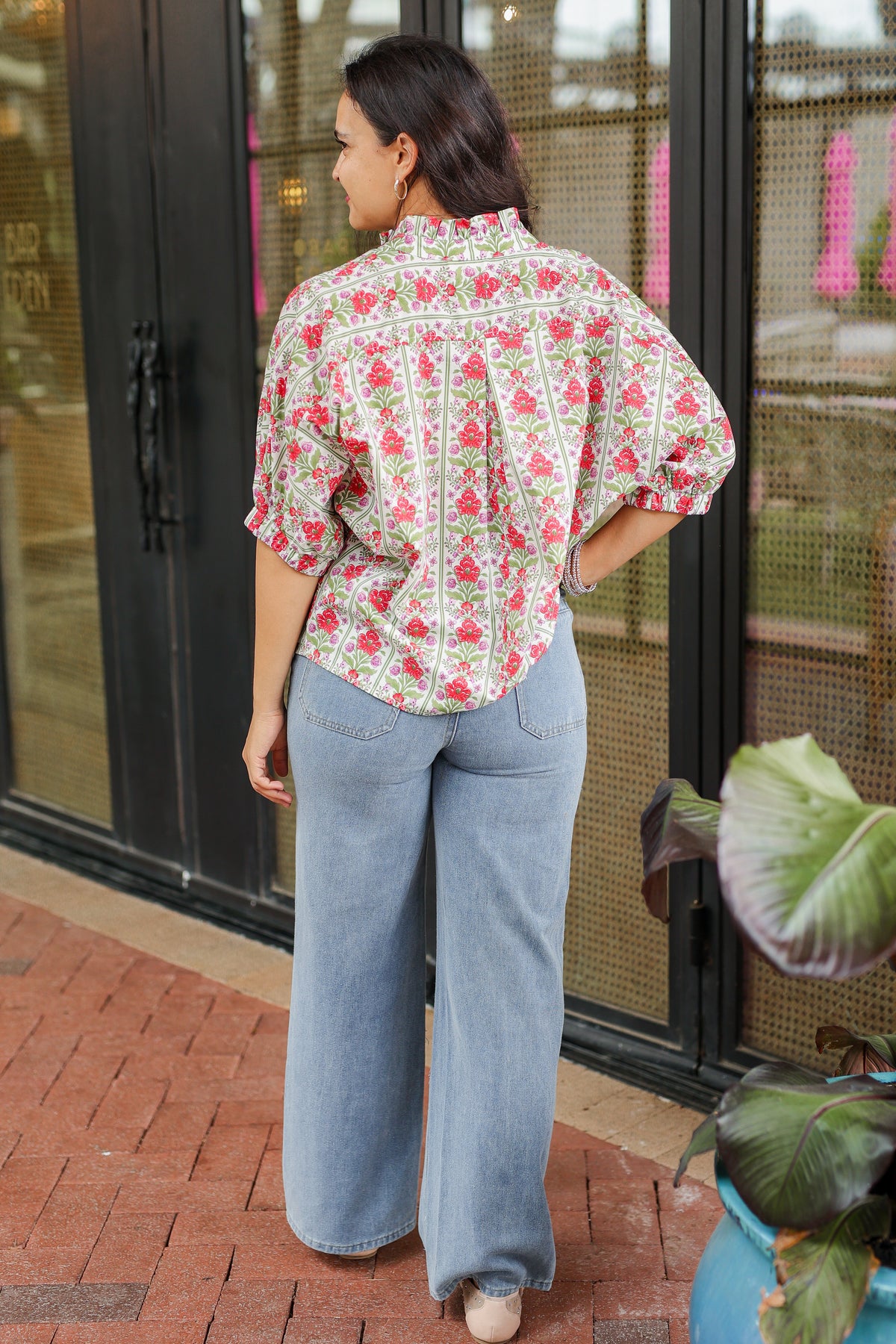 Woman wearing a floral blouse and jeans standing in front of a glass door.