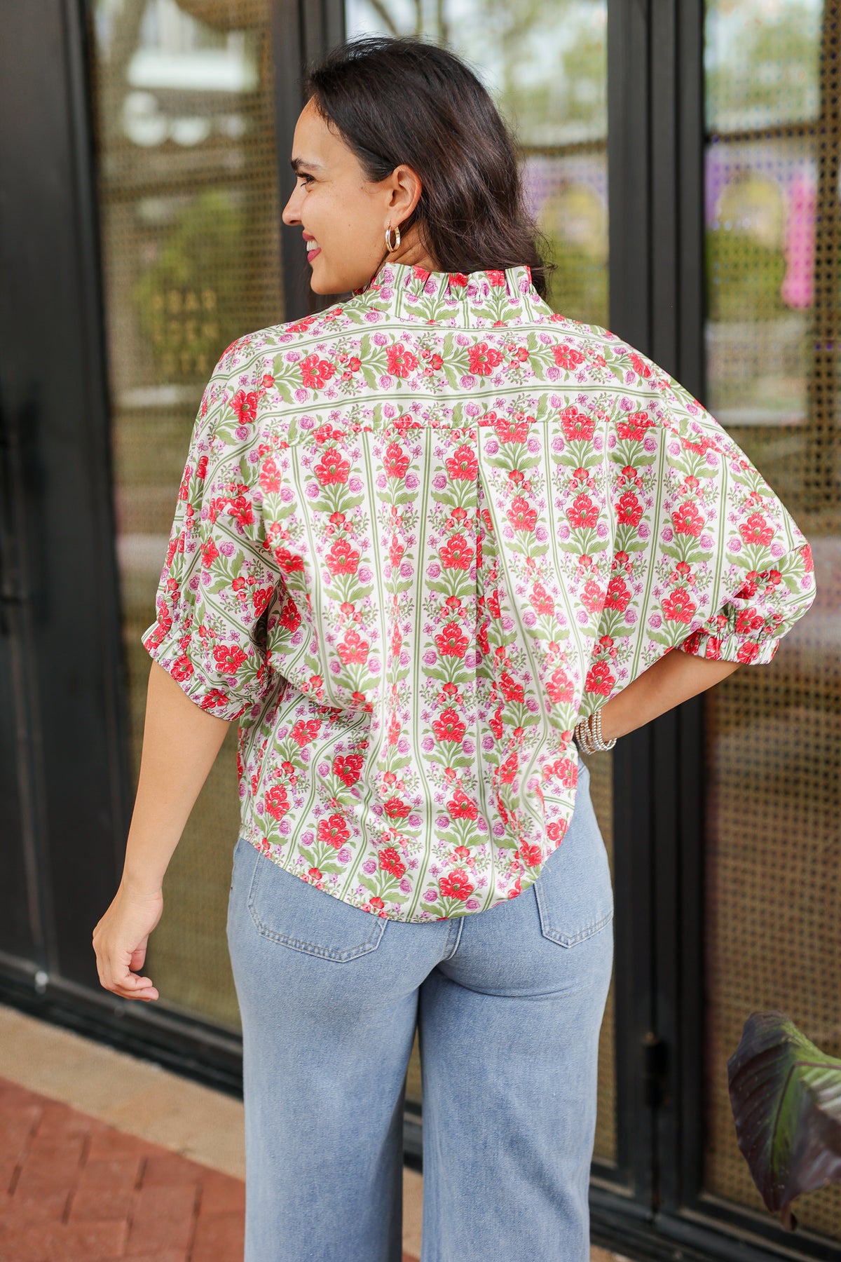 Woman wearing a floral blouse and jeans standing in front of a glass door.