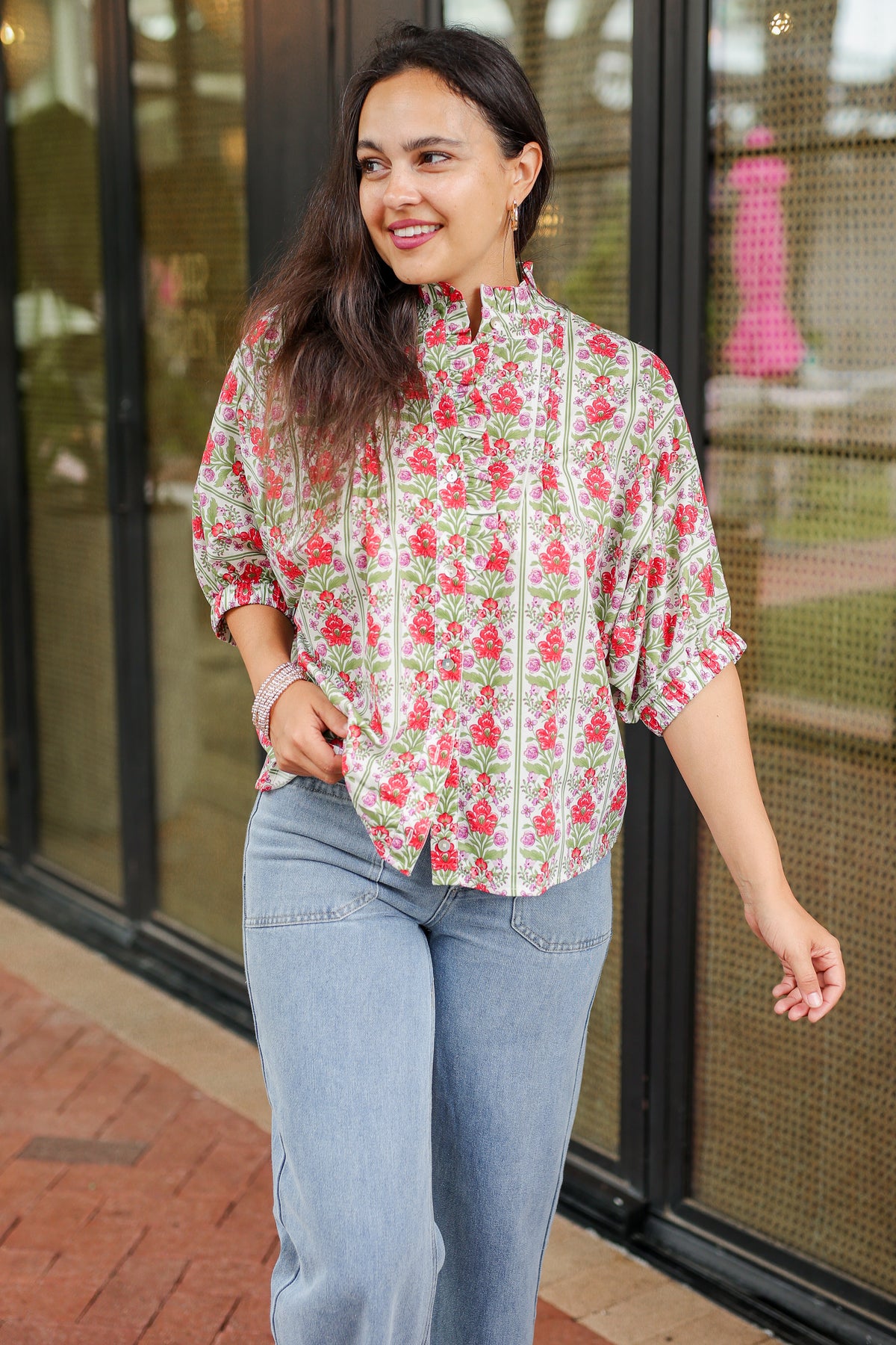 Woman wearing a floral blouse and jeans walking outdoors.