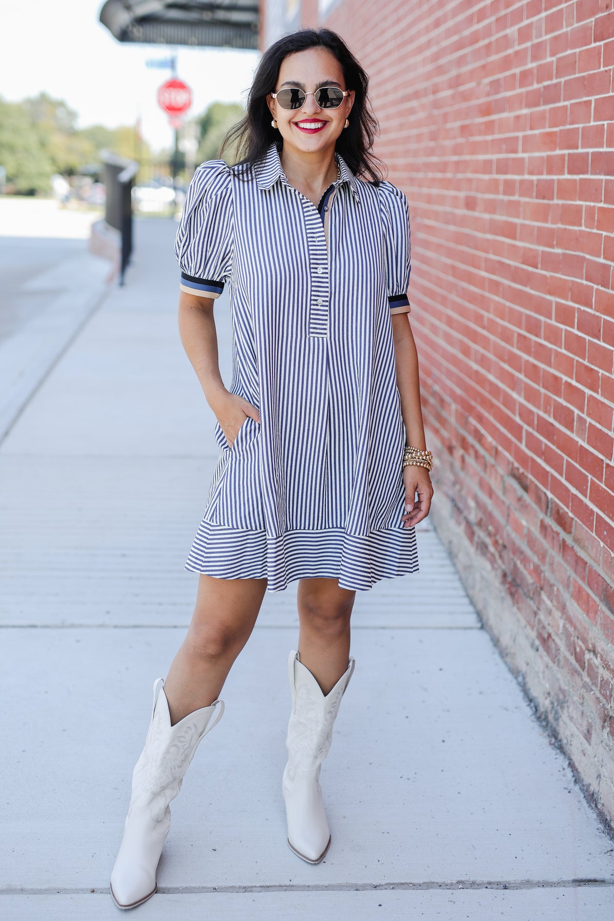 Woman wearing a striped dress and white boots on a sidewalk.