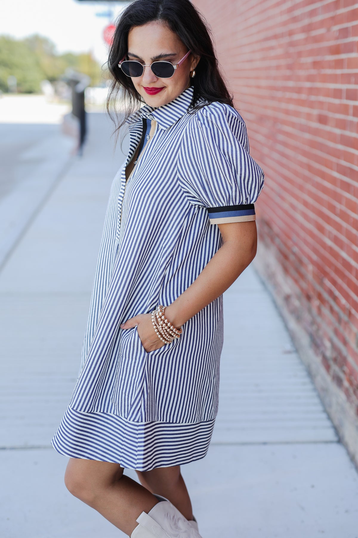 Woman wearing a blue and white striped dress on a sidewalk with a brick wall in the background.