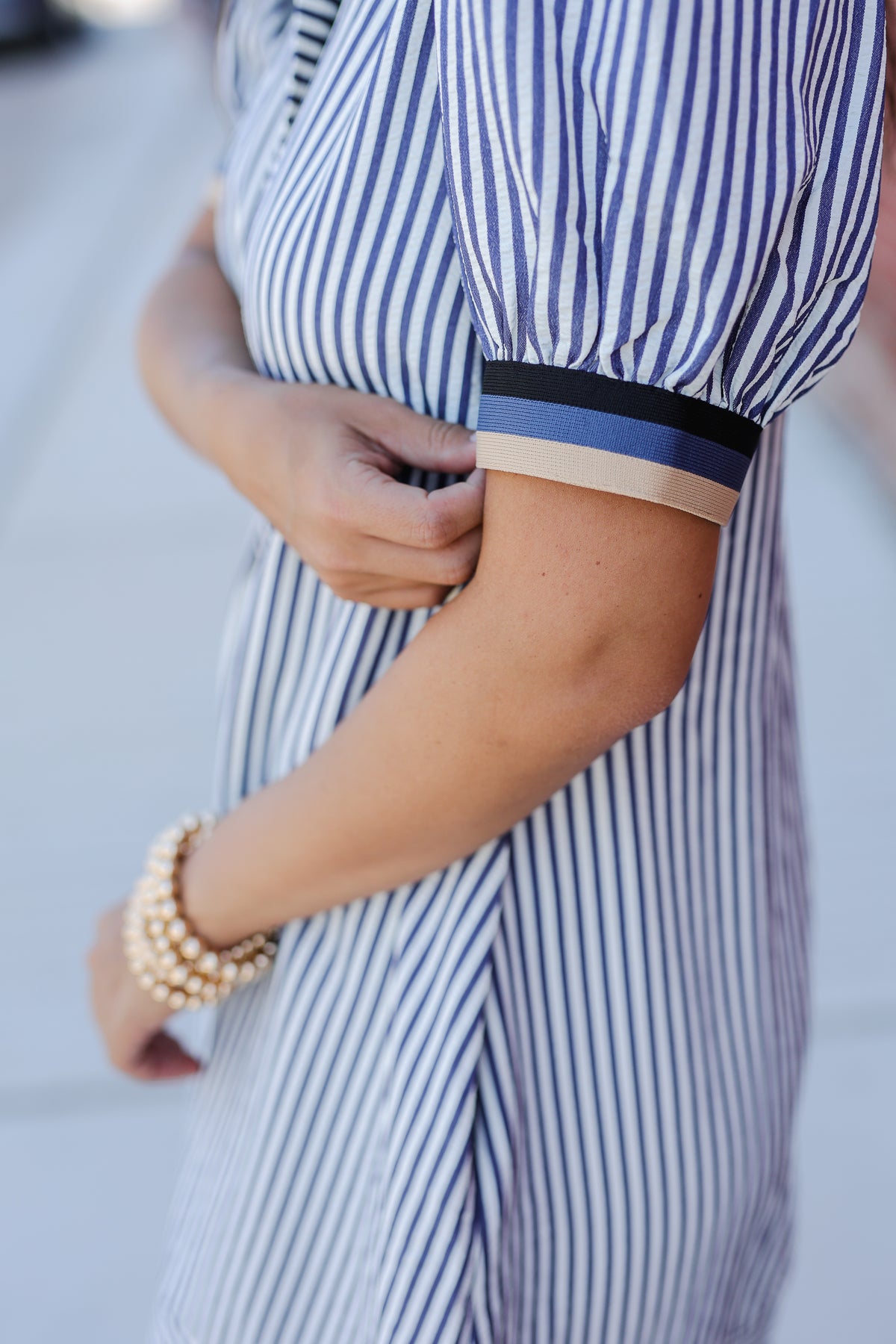 Close-up of a person wearing a blue and white striped dress with a bracelet on a blurred background