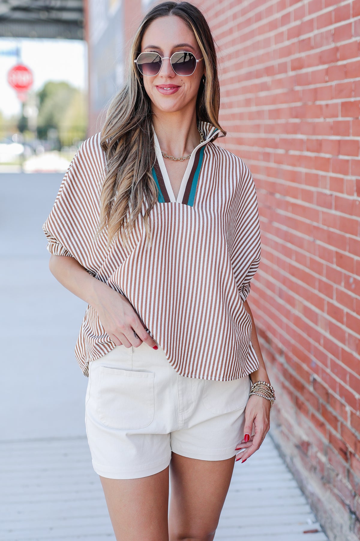 Woman wearing a striped shirt and white shorts standing against a brick wall.