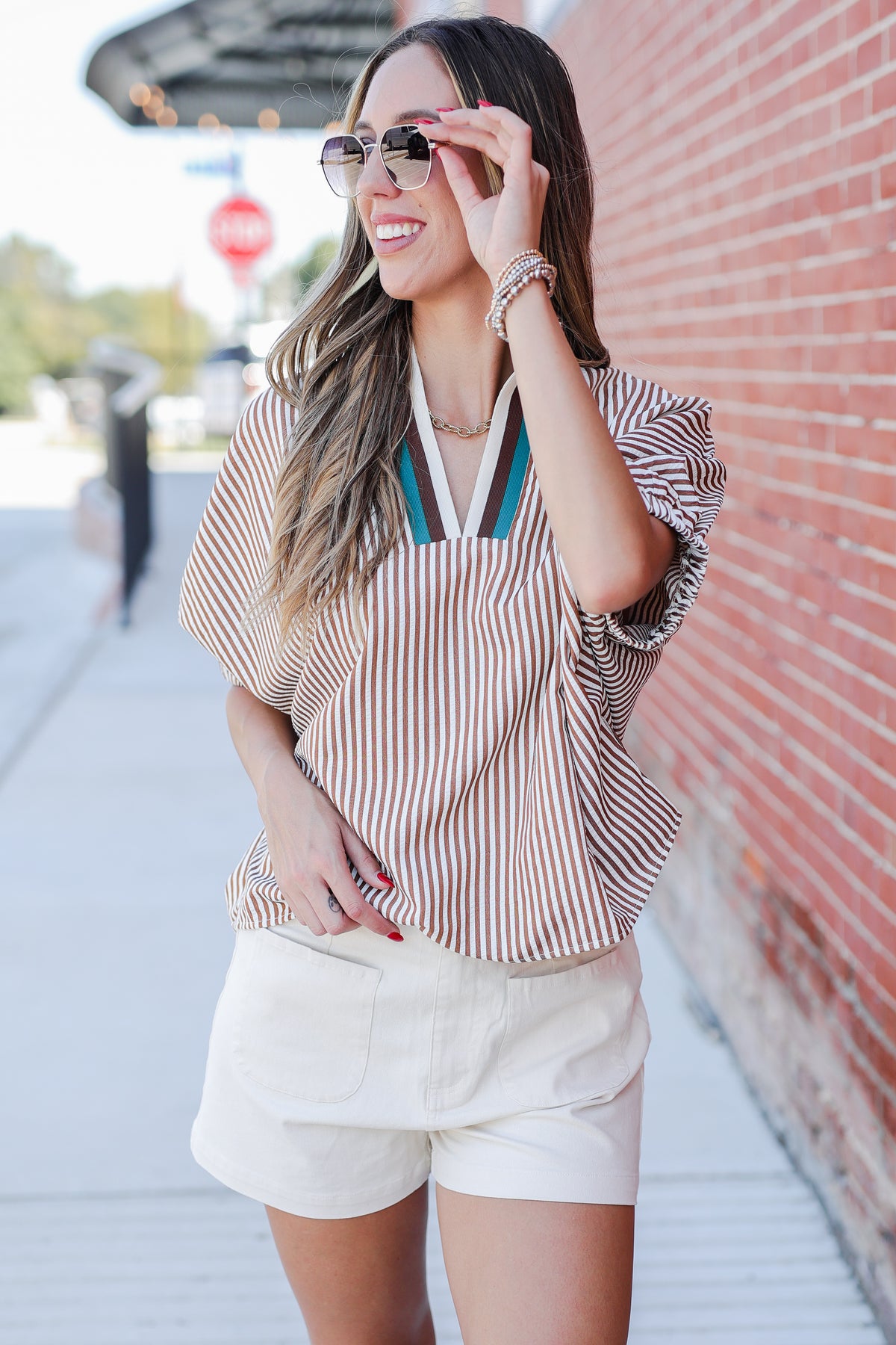 Woman wearing a striped shirt and white shorts standing against a brick wall.
