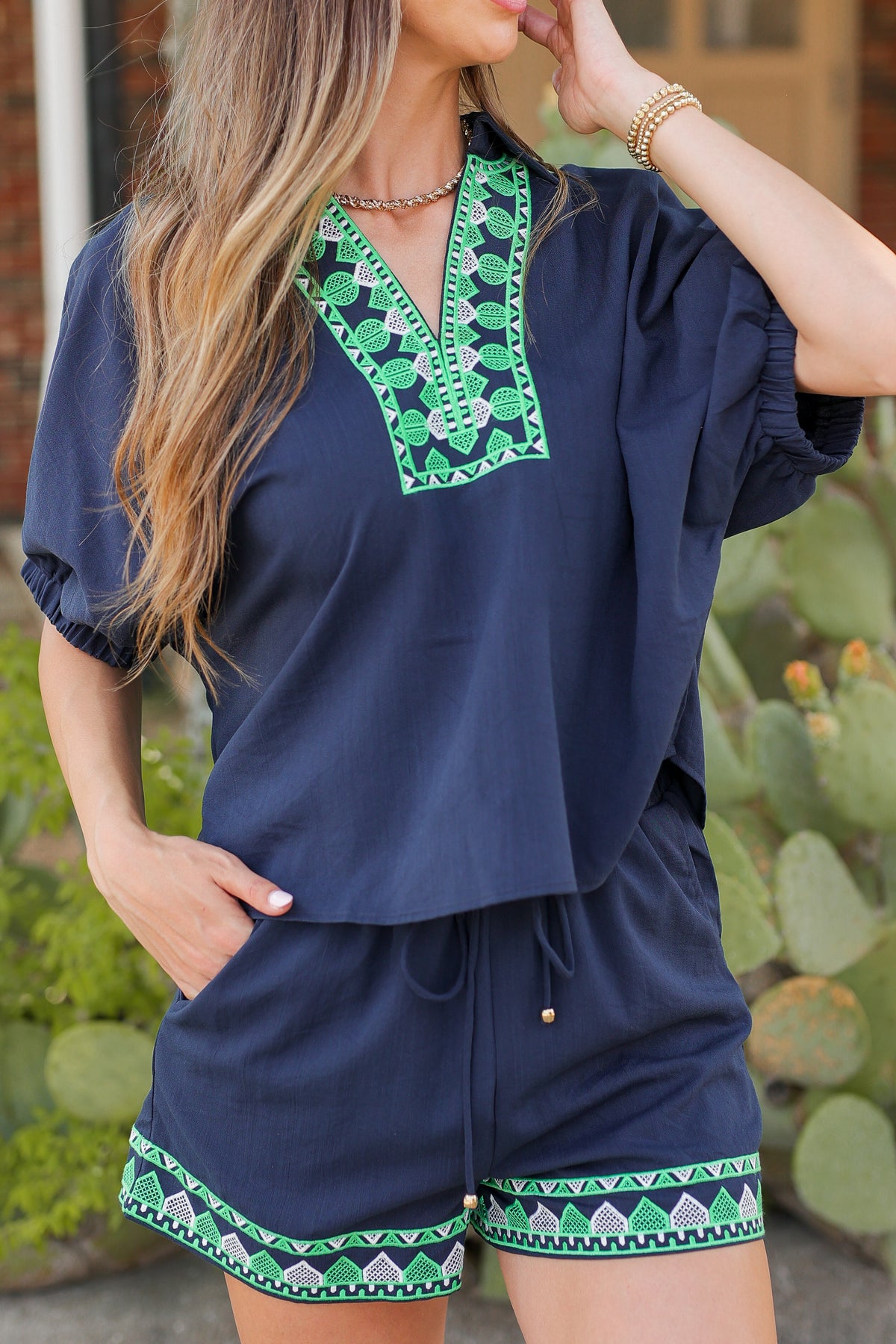 Woman wearing a navy blue outfit with green patterns in front of cacti.