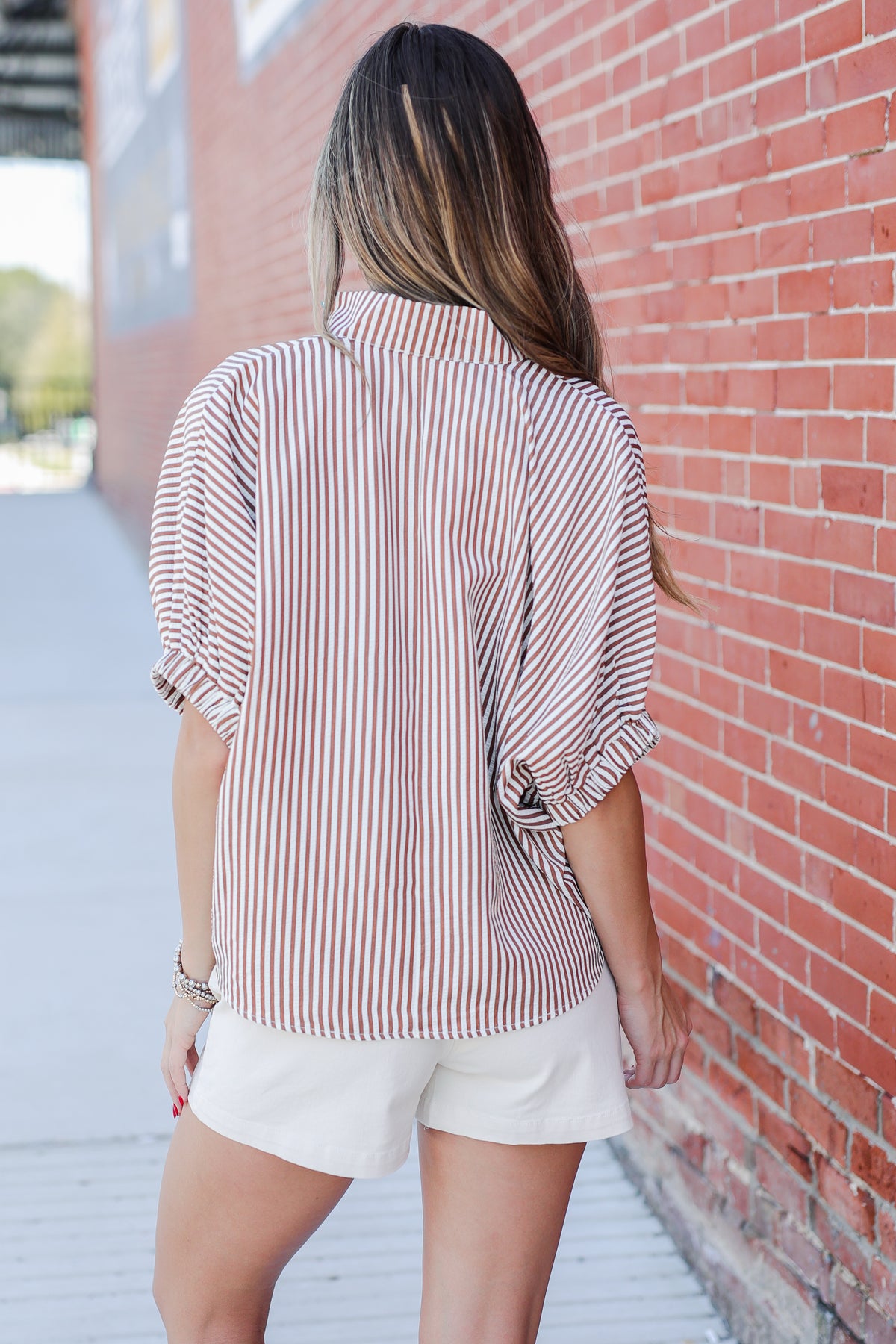 Person wearing a striped shirt and white shorts against a brick wall.