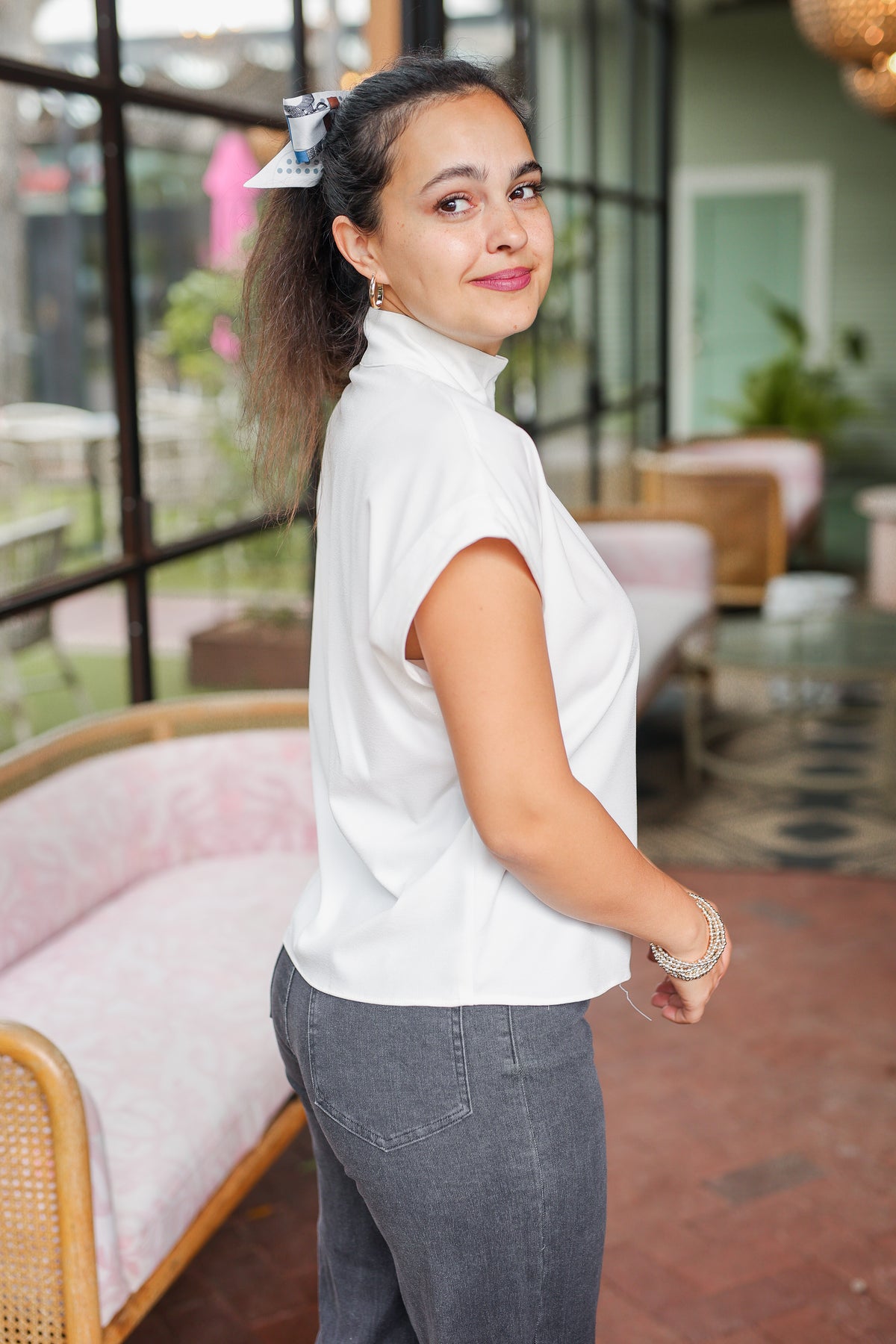 Woman in a white blouse and gray pants standing in an indoor setting with a blurred background