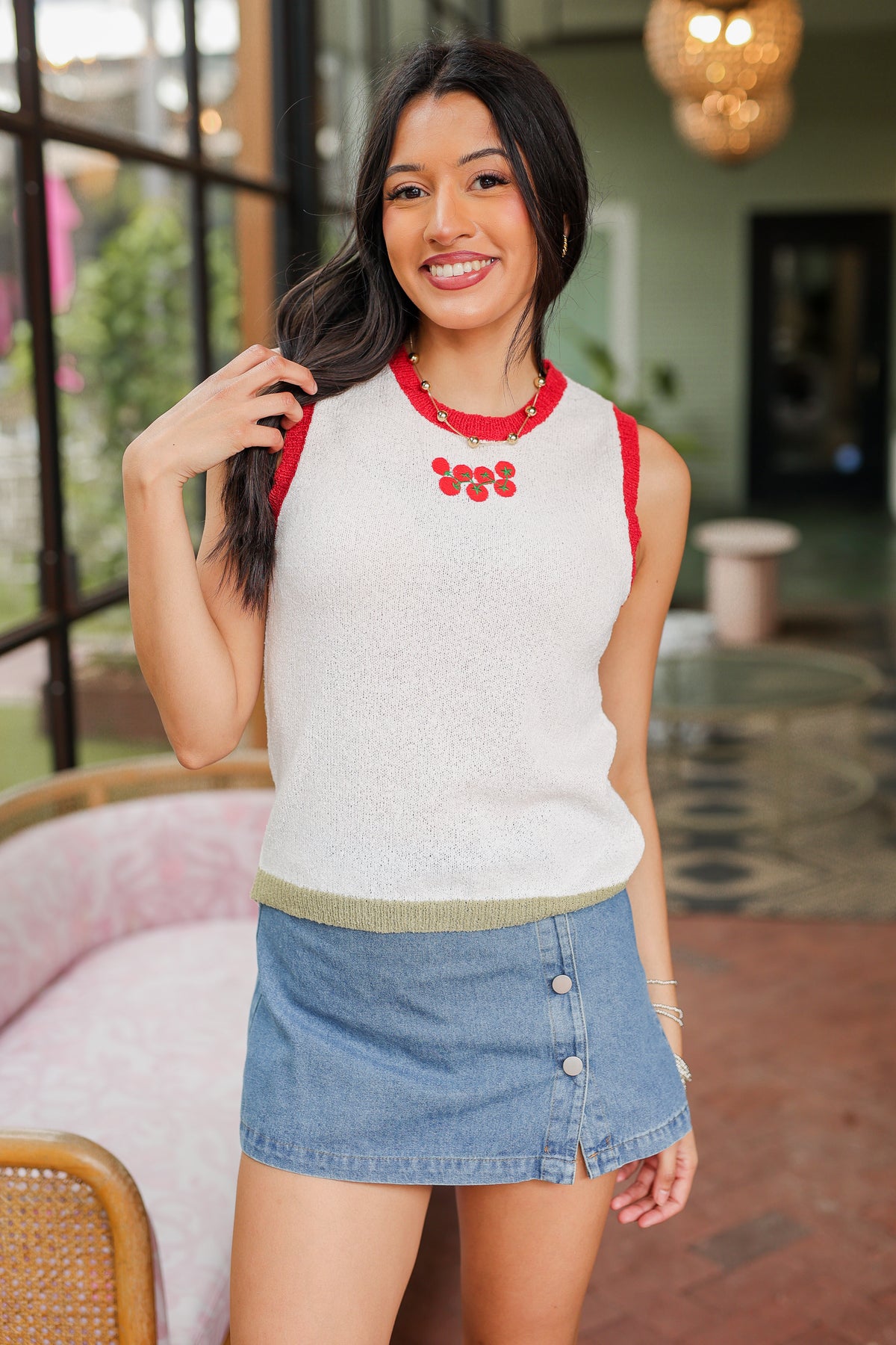 Woman wearing a sleeveless top with red trim and a denim skirt in an outdoor setting.