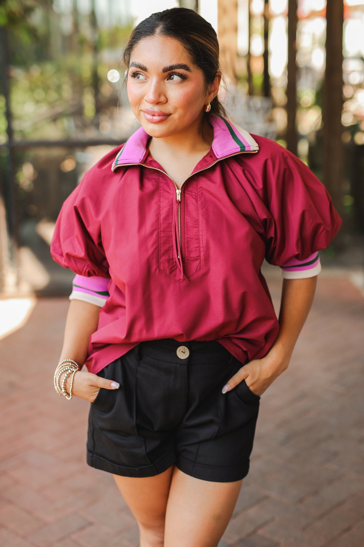 Woman wearing a red jacket with pink trim and black shorts outdoors.