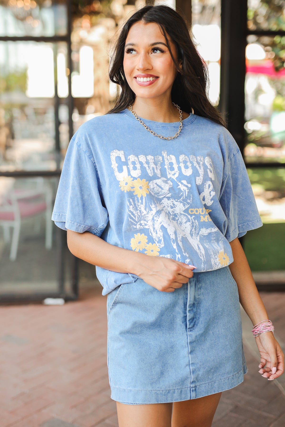 Woman wearing a blue graphic t-shirt and denim skirt outdoors