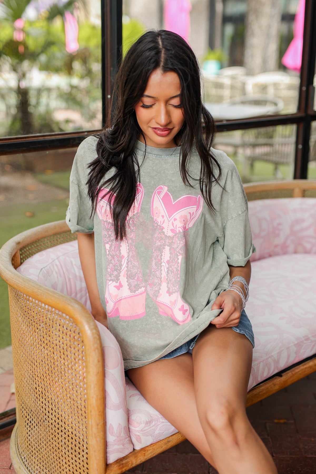 Woman sitting on a wicker chair wearing a gray t-shirt with pink designs.