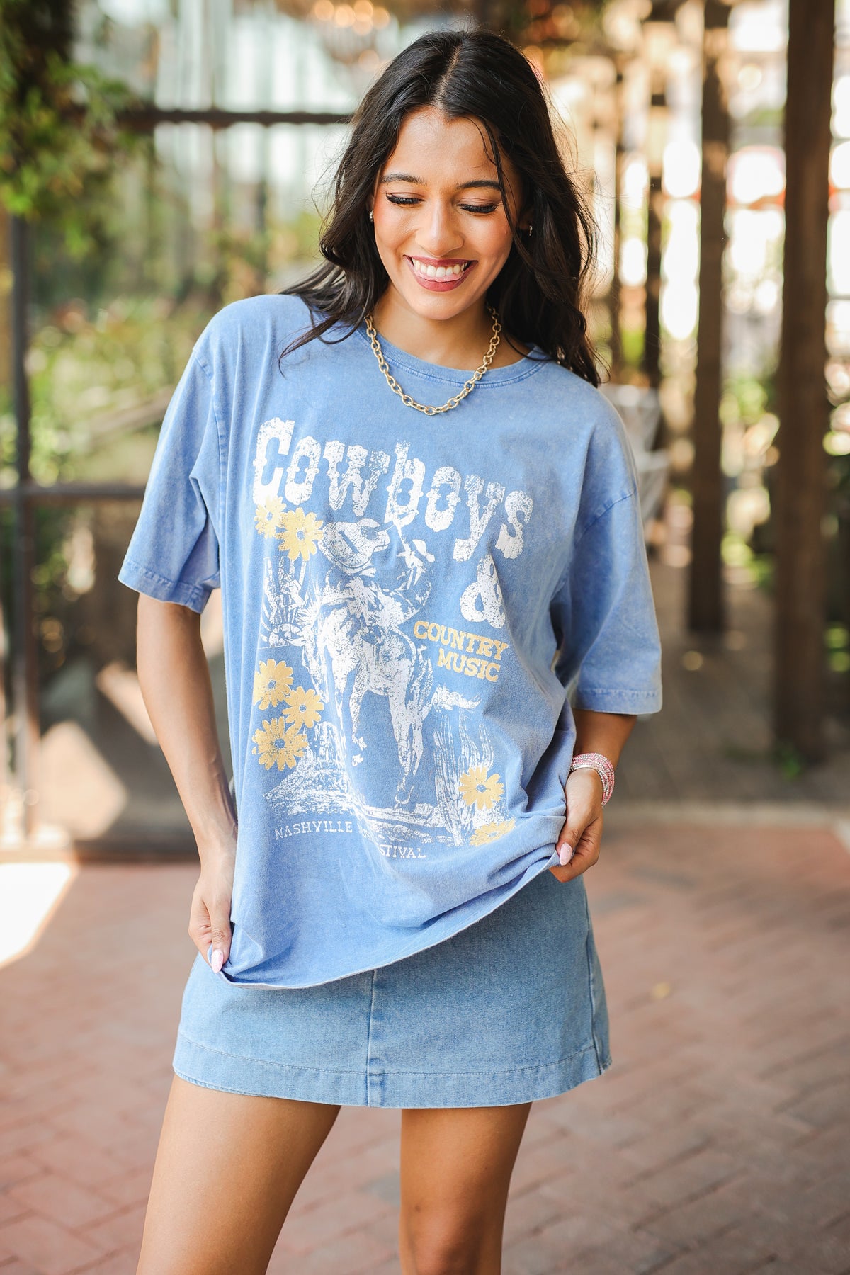 Woman wearing a blue graphic t-shirt with 'Cowboys' and 'Country music' text outdoors.