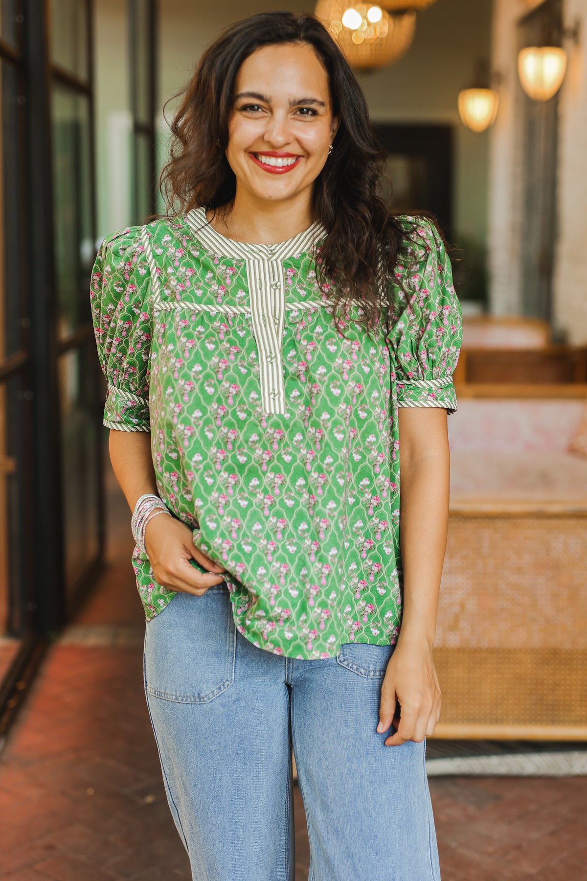 Woman wearing a green floral blouse and blue jeans standing in an outdoor setting.