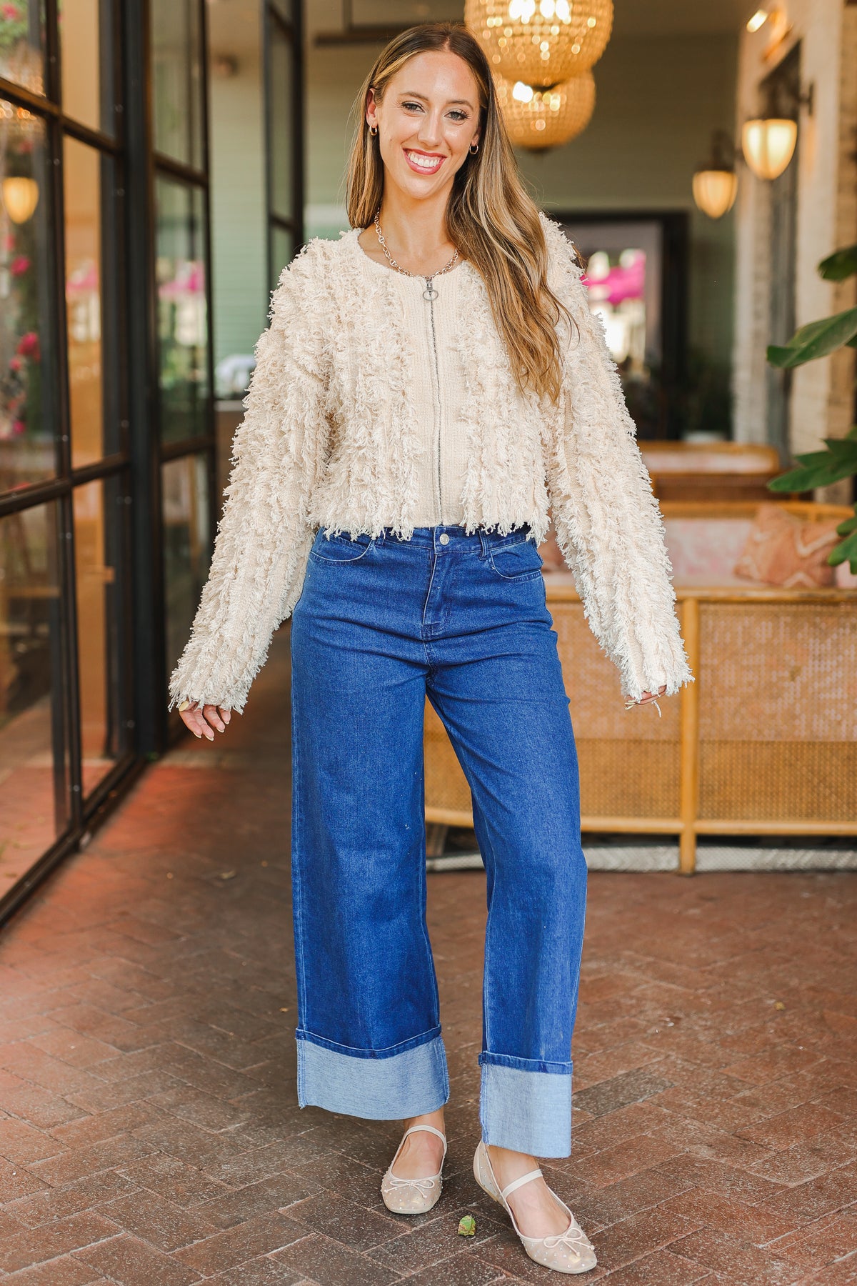 Woman wearing a textured white top and blue jeans standing in an outdoor setting.