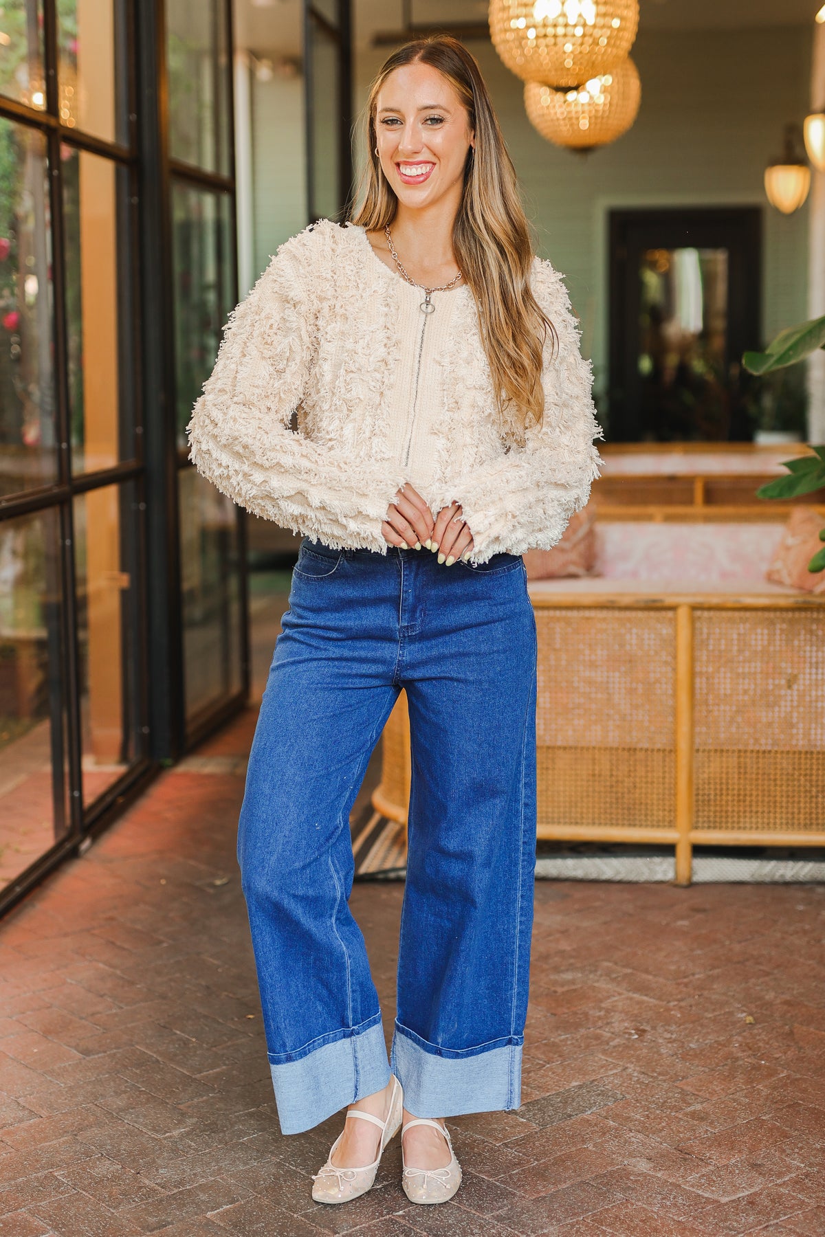Woman wearing a textured white top and blue jeans standing in an indoor setting.