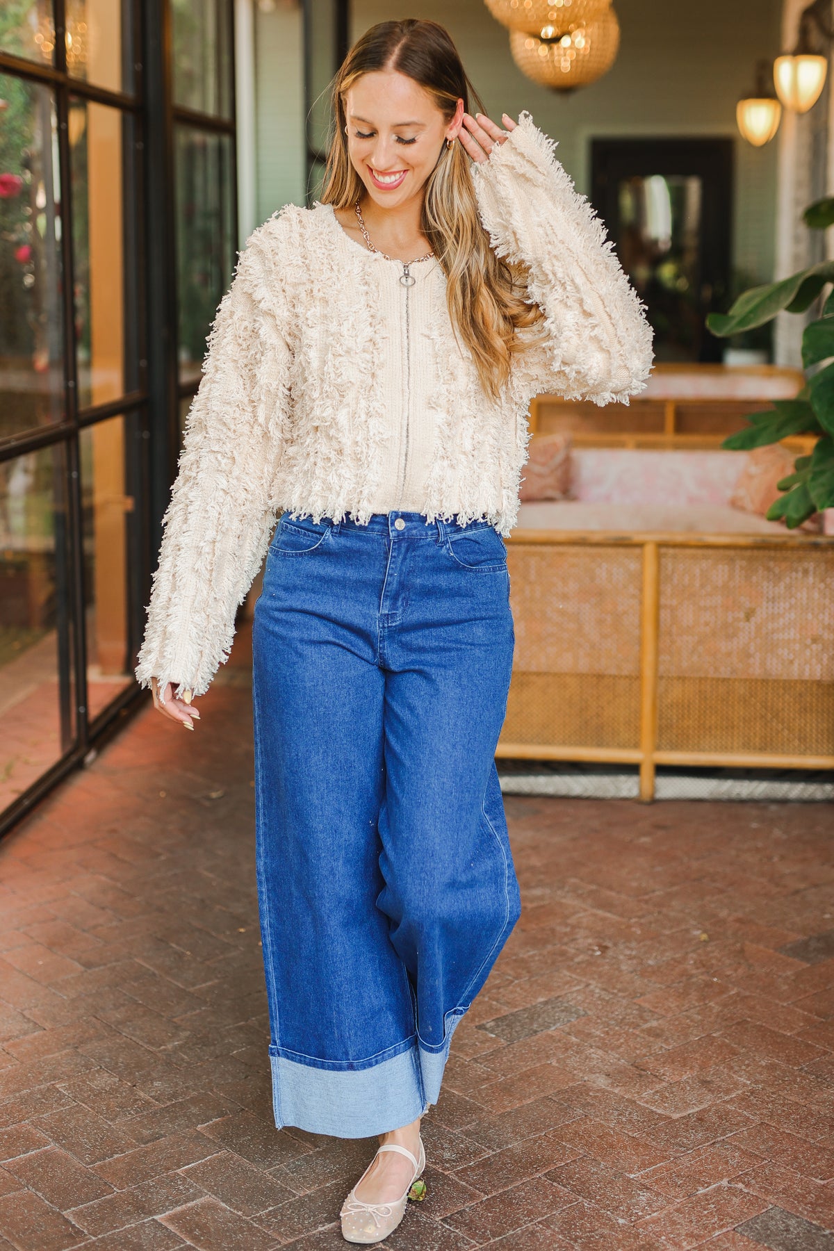 Woman wearing a white textured sweater and blue jeans in an indoor setting.