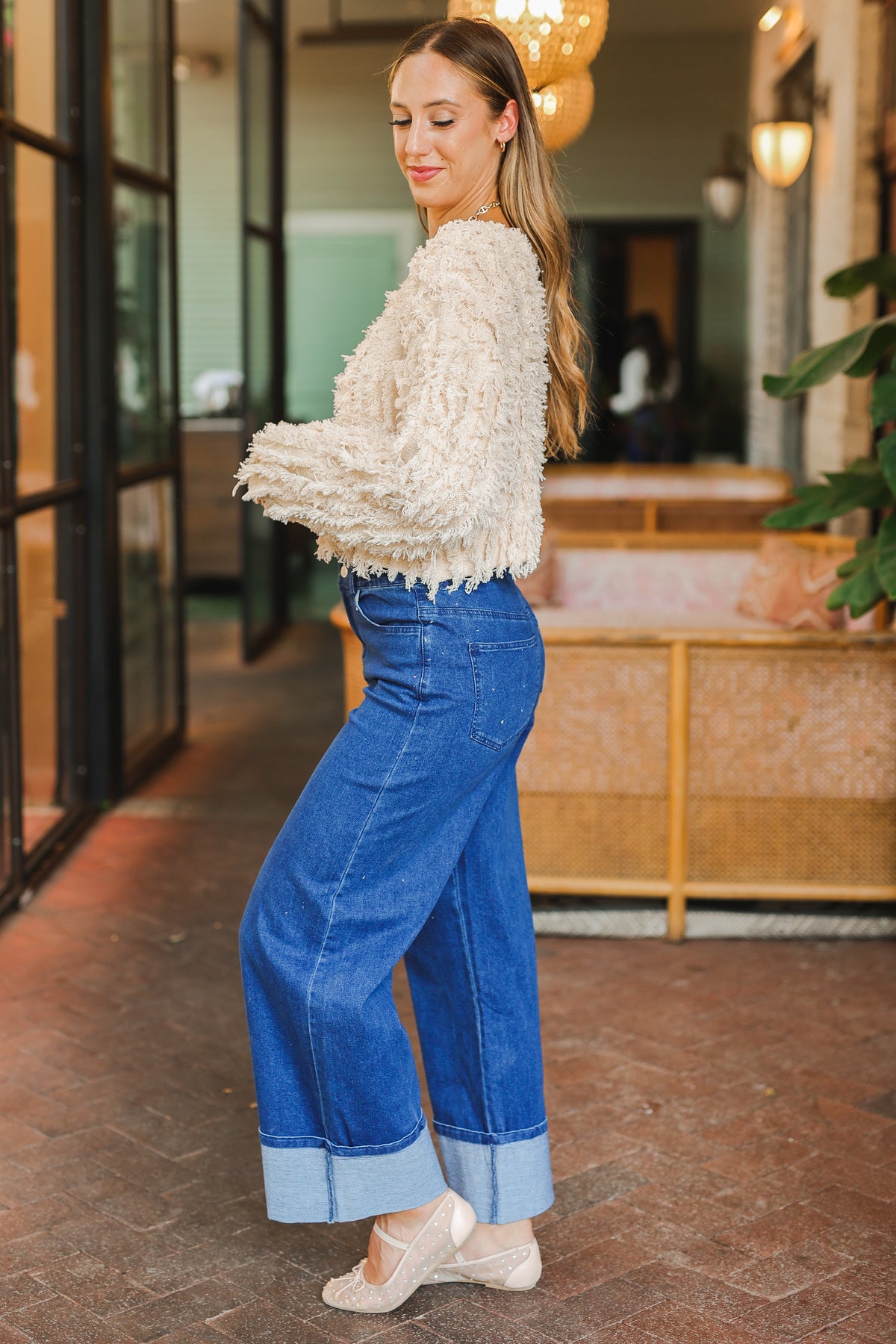 Woman wearing a textured white sweater and blue jeans standing in an indoor setting.
