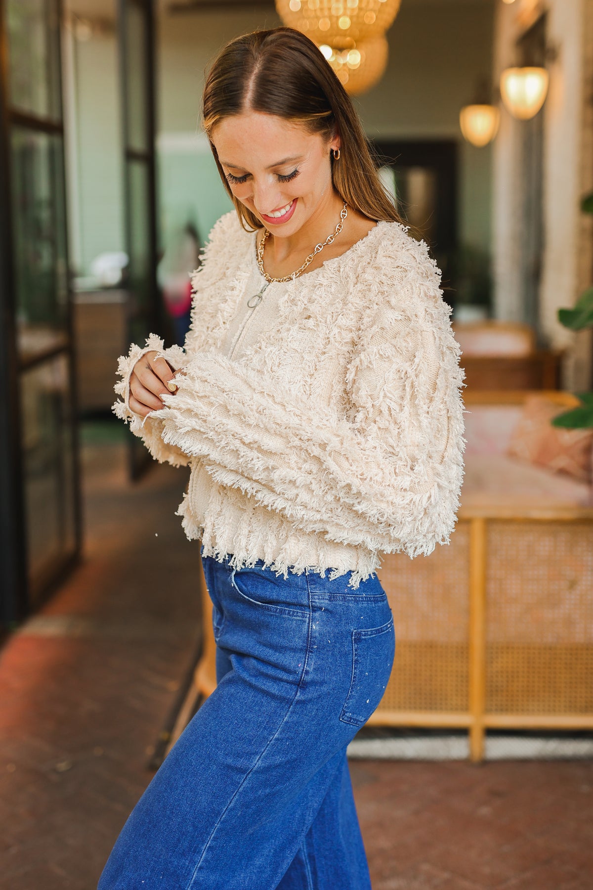 Woman wearing a cream sweater and blue jeans in an indoor setting
