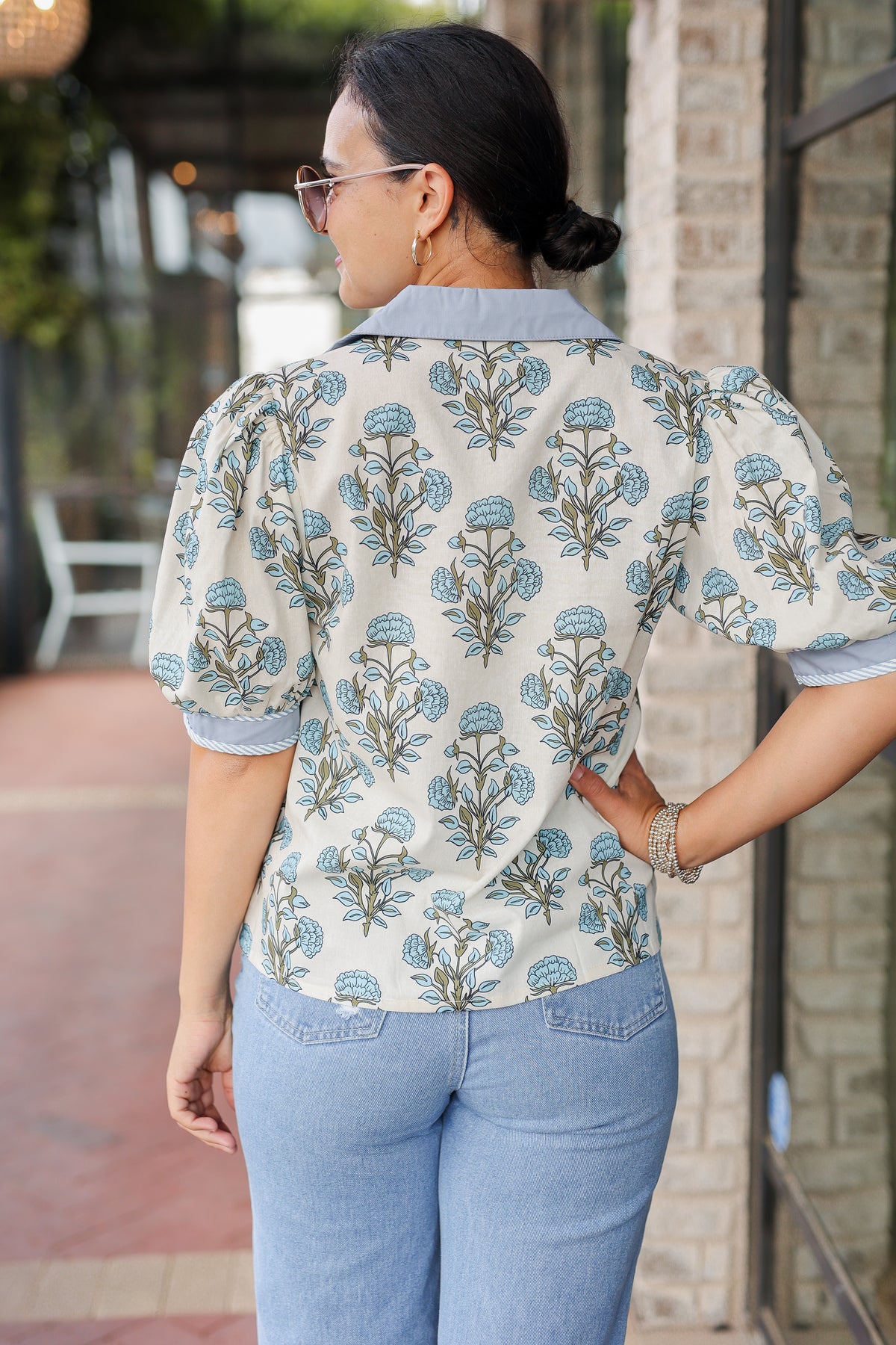Woman wearing a floral blouse and light blue jeans outdoors.