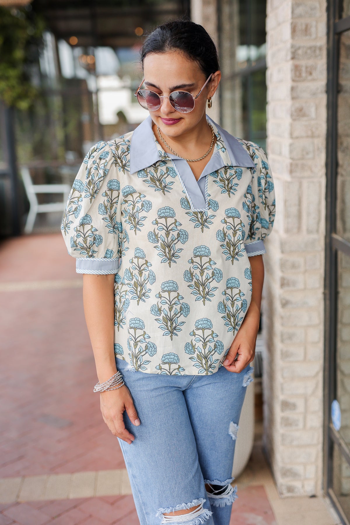 Woman wearing a floral blouse and jeans standing on a sidewalk.