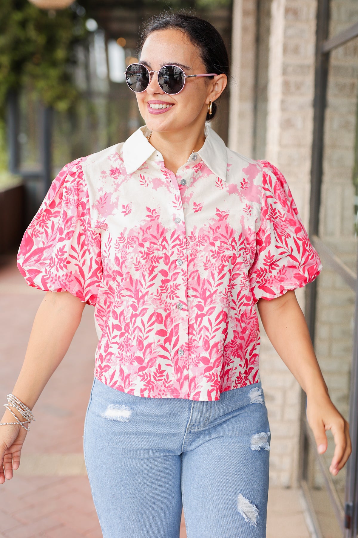 Woman wearing a pink floral blouse and blue jeans outdoors.
