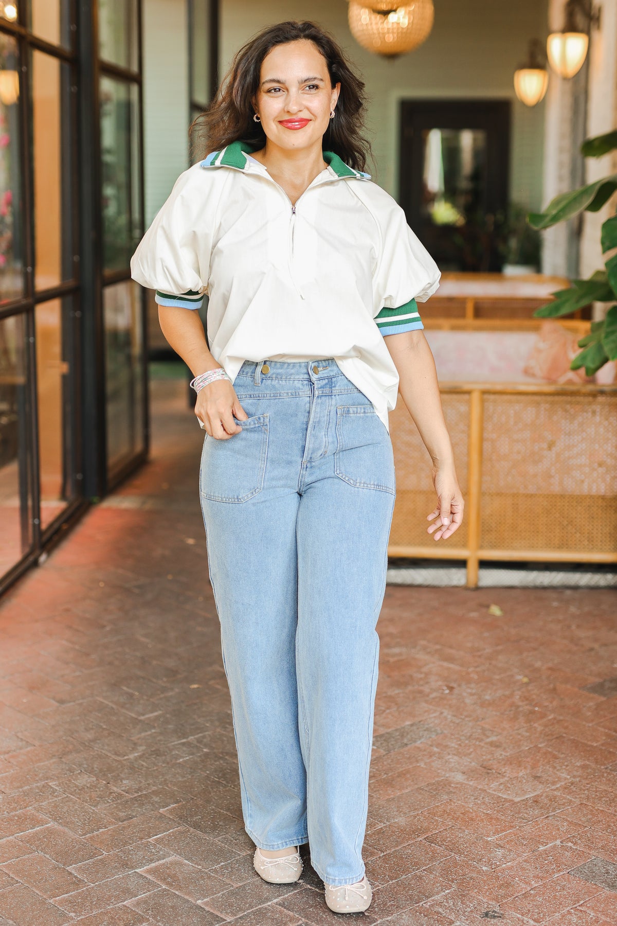 Woman wearing a white shirt with green accents and blue jeans standing outdoors.