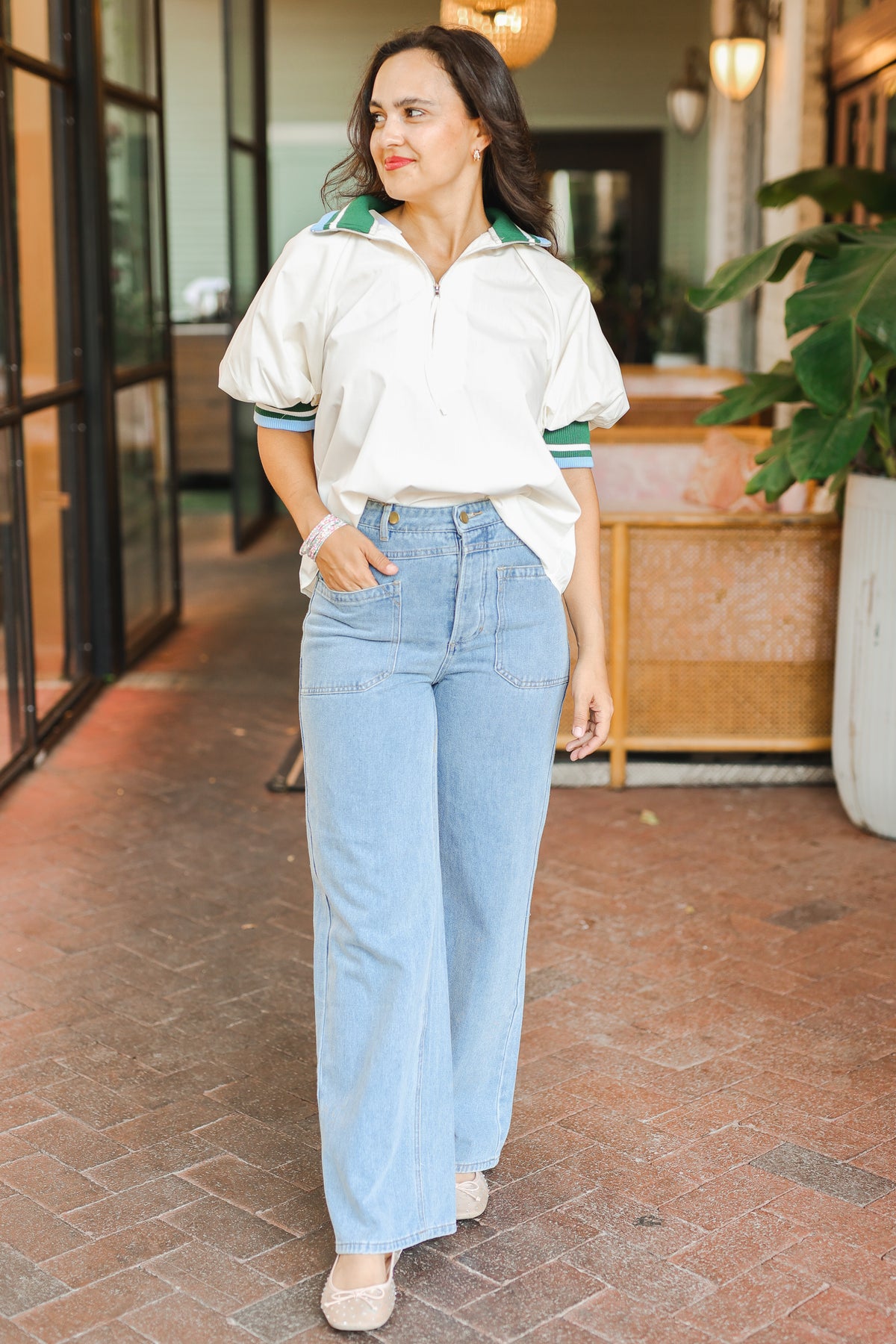 Woman wearing a white polo shirt with green accents and light blue jeans, standing in an outdoor setting.
