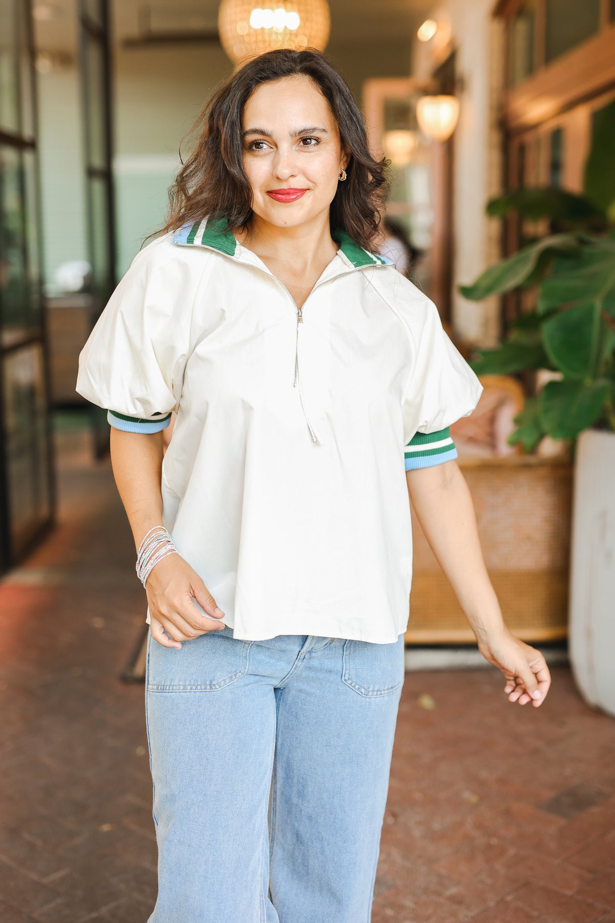 Woman wearing a white shirt with green accents and blue jeans outdoors.