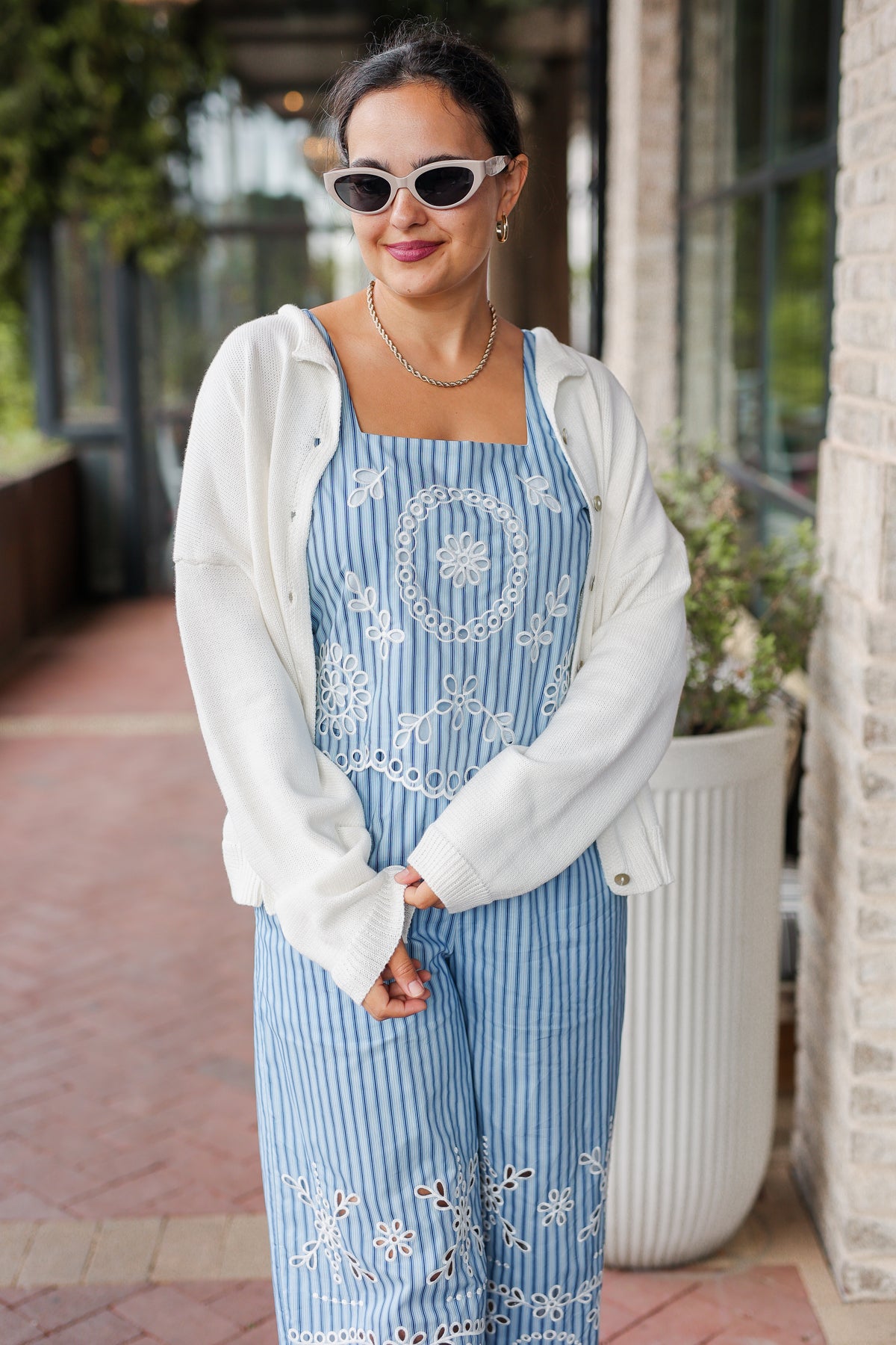 Woman wearing a blue striped dress with white embroidery and a white cardigan outdoors.