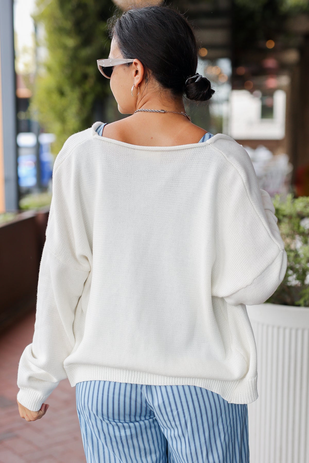 Person wearing a white sweater and blue striped pants on a blurred outdoor background