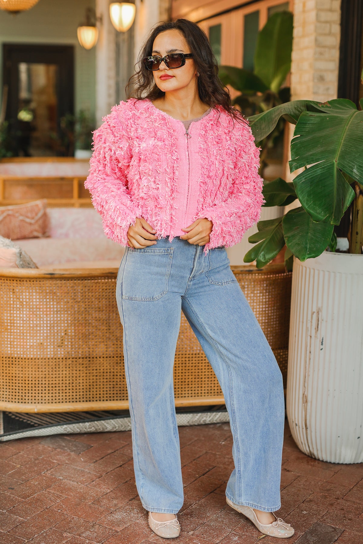 Woman wearing a pink sequin jacket and blue jeans standing in an outdoor setting.